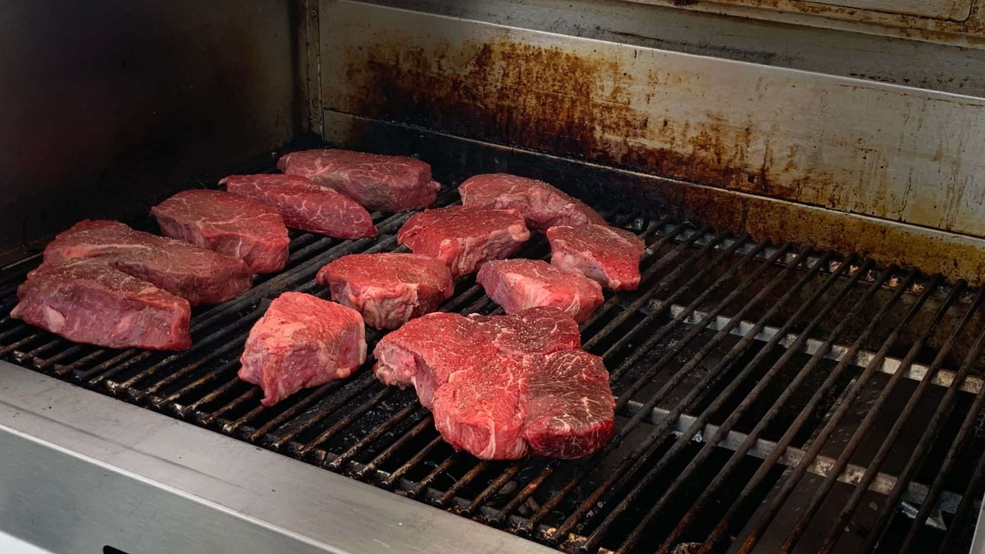 Large raw beef steaks are grilling on a food cart grill.