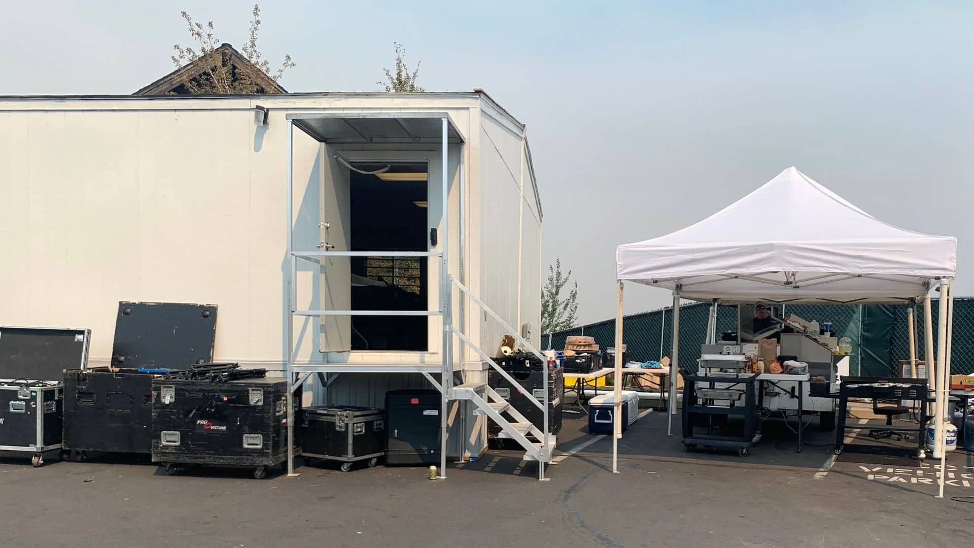 Bruneau's food cart under a white tent appears on a film set with production equipment, including black cases, tables, and supplies, on a paved area.