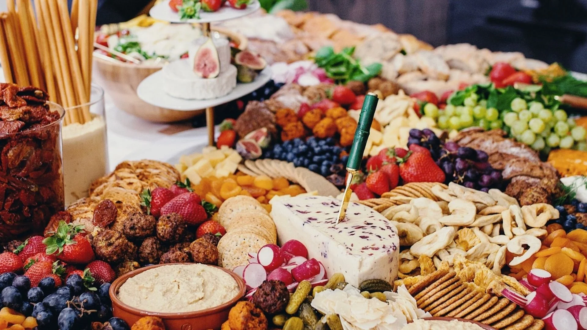 A colorful beautiful "Grazing Table" is spread on a long table with various cheeses, fruits, crackers, and appetizers for a wedding.