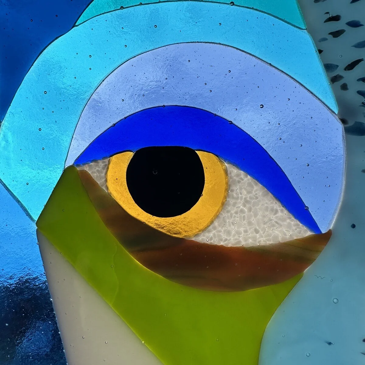 Abstract glass sculpture resembling an eye with layered colors including blue, yellow, green, white, and black.