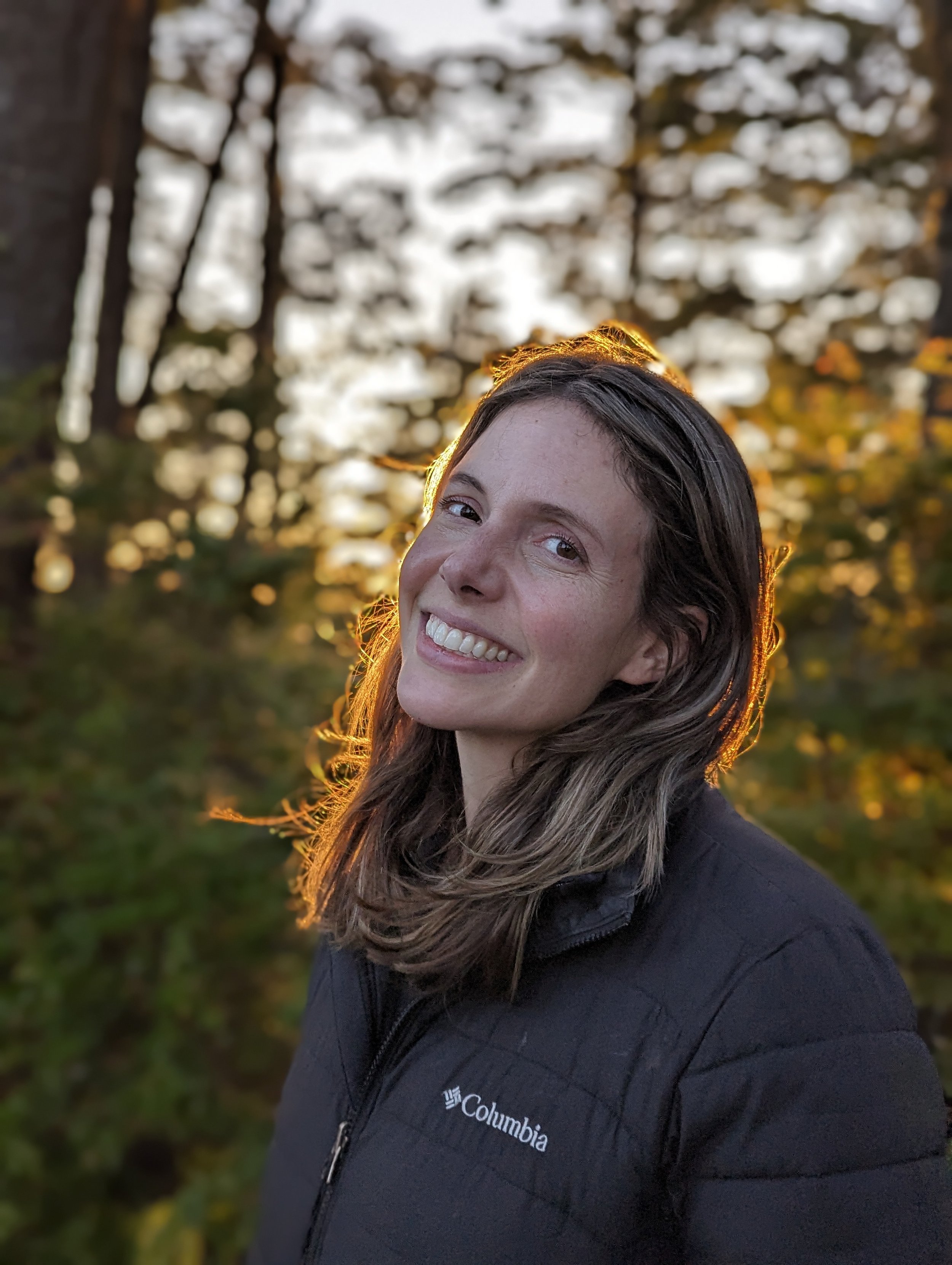 headshot of the author standing in front of a forested area during the golden hour.