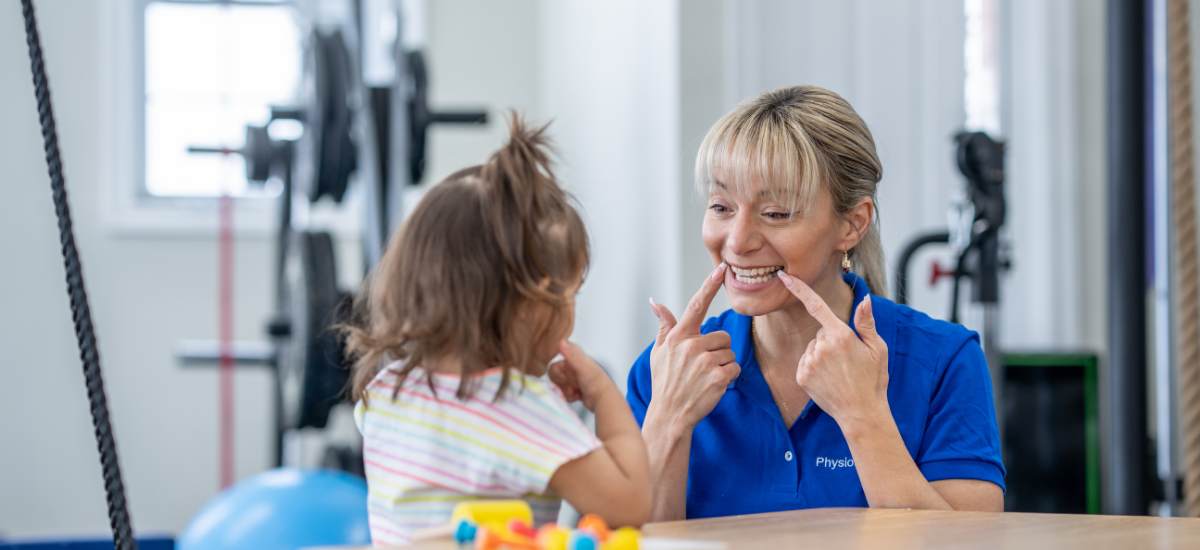 Therapist in blue shirt engaging with young girl during therapy session in a rehab gym