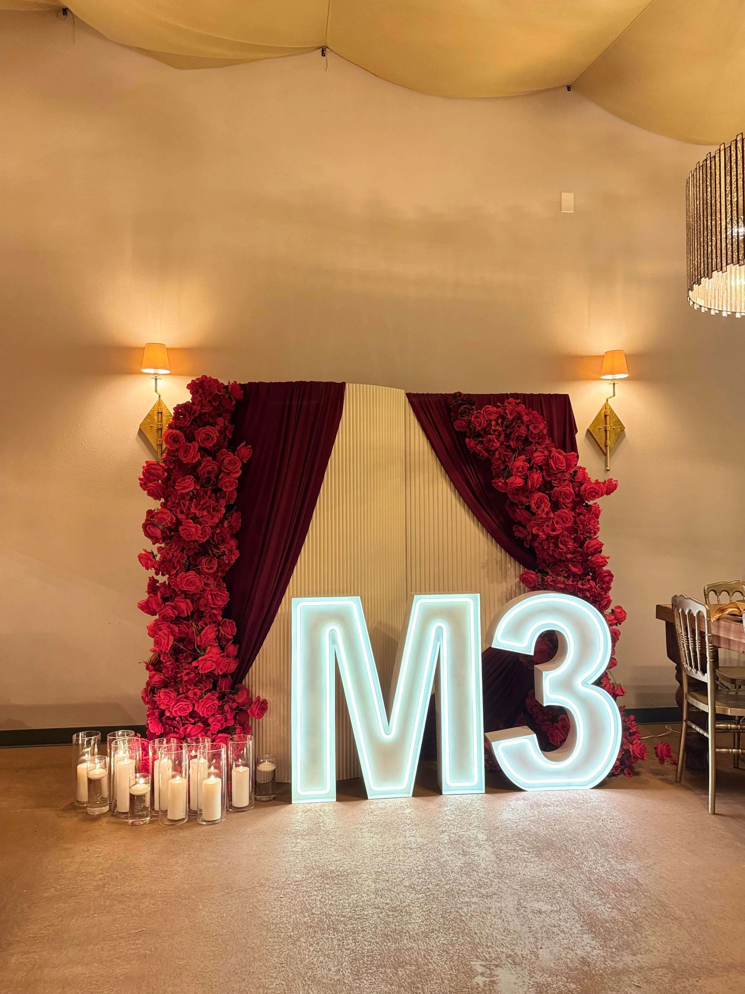 Glowing M3 LED marquee letters in front of red rose backdrop.