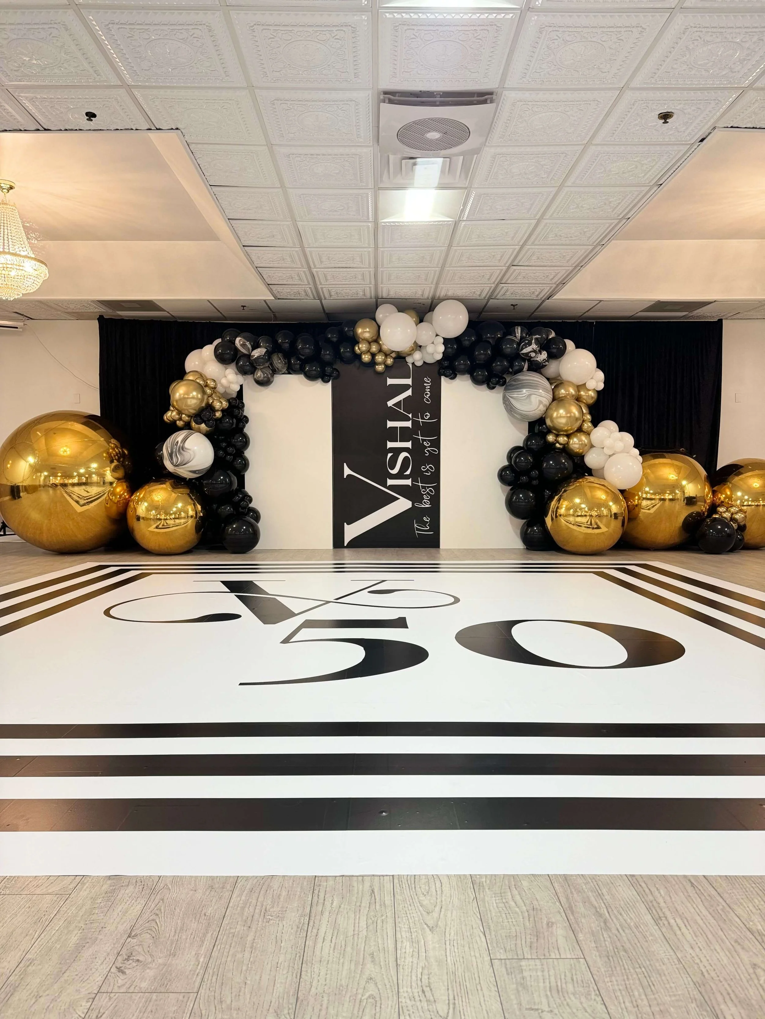 Luxury black, white, and gold 50th birthday balloon setup with personalized signage.