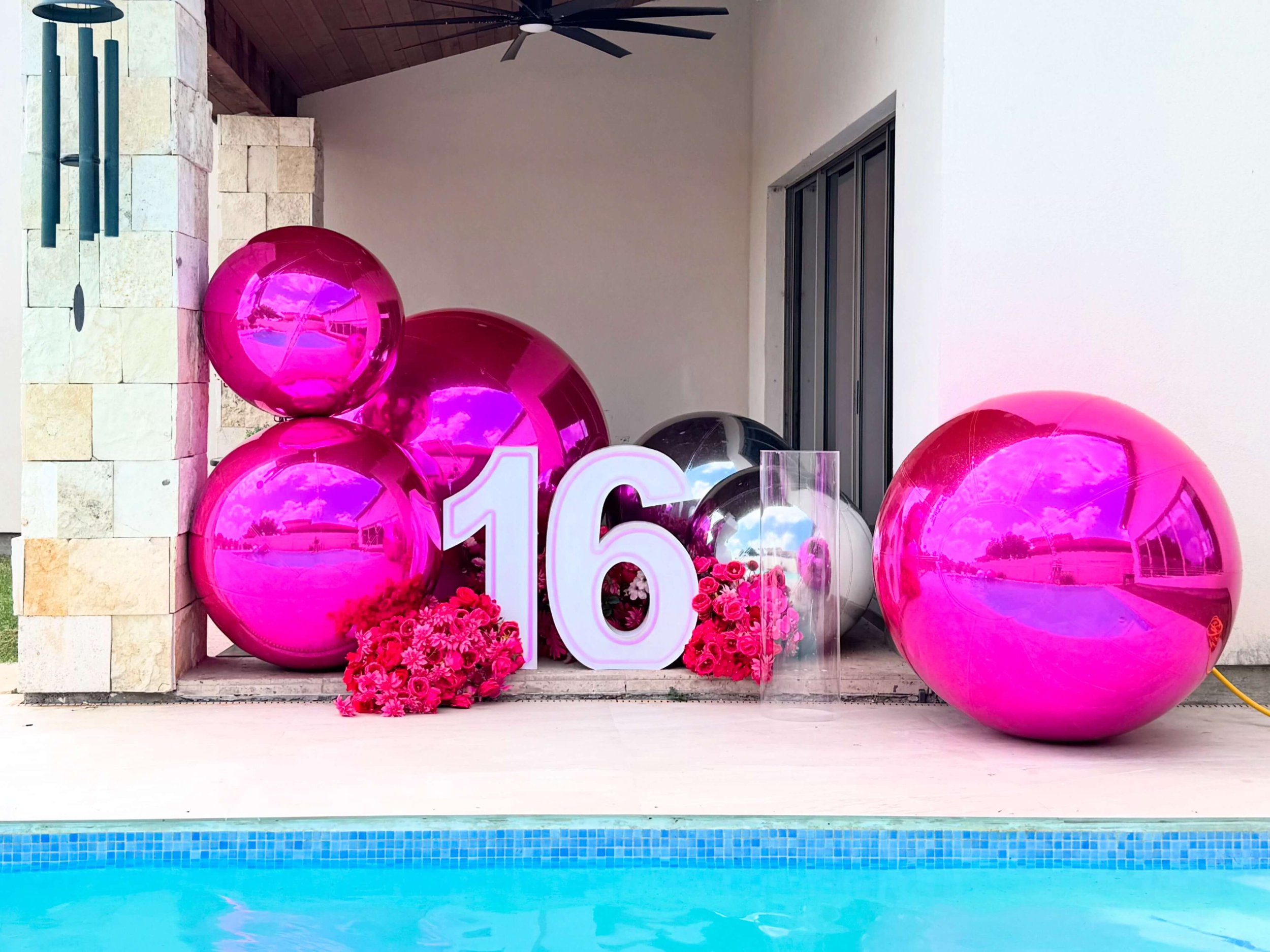 Sweet 16 event décor featuring illuminated LED marquee number 16, surrounded by oversized pink chrome spheres and floral accents, displayed poolside for a luxury birthday celebration.