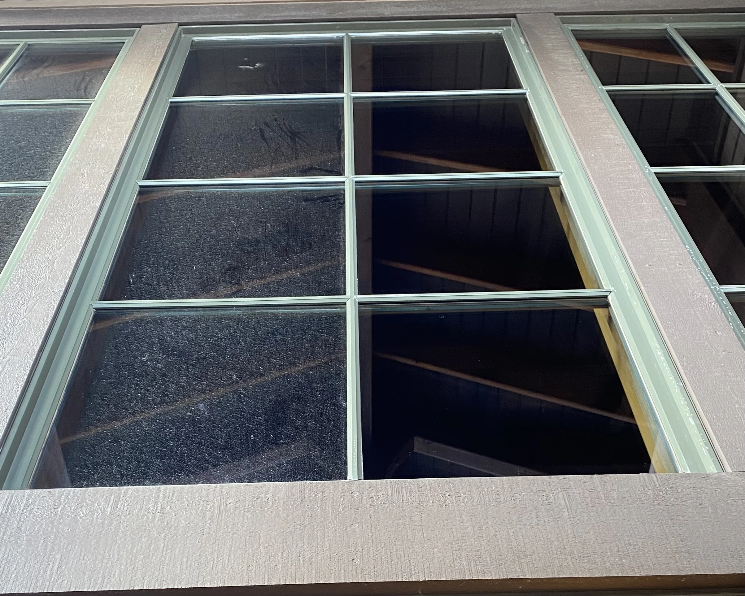 Close-up of a window with multiple panes, green frame, and a beige textured wall, taken from a low angle at night.