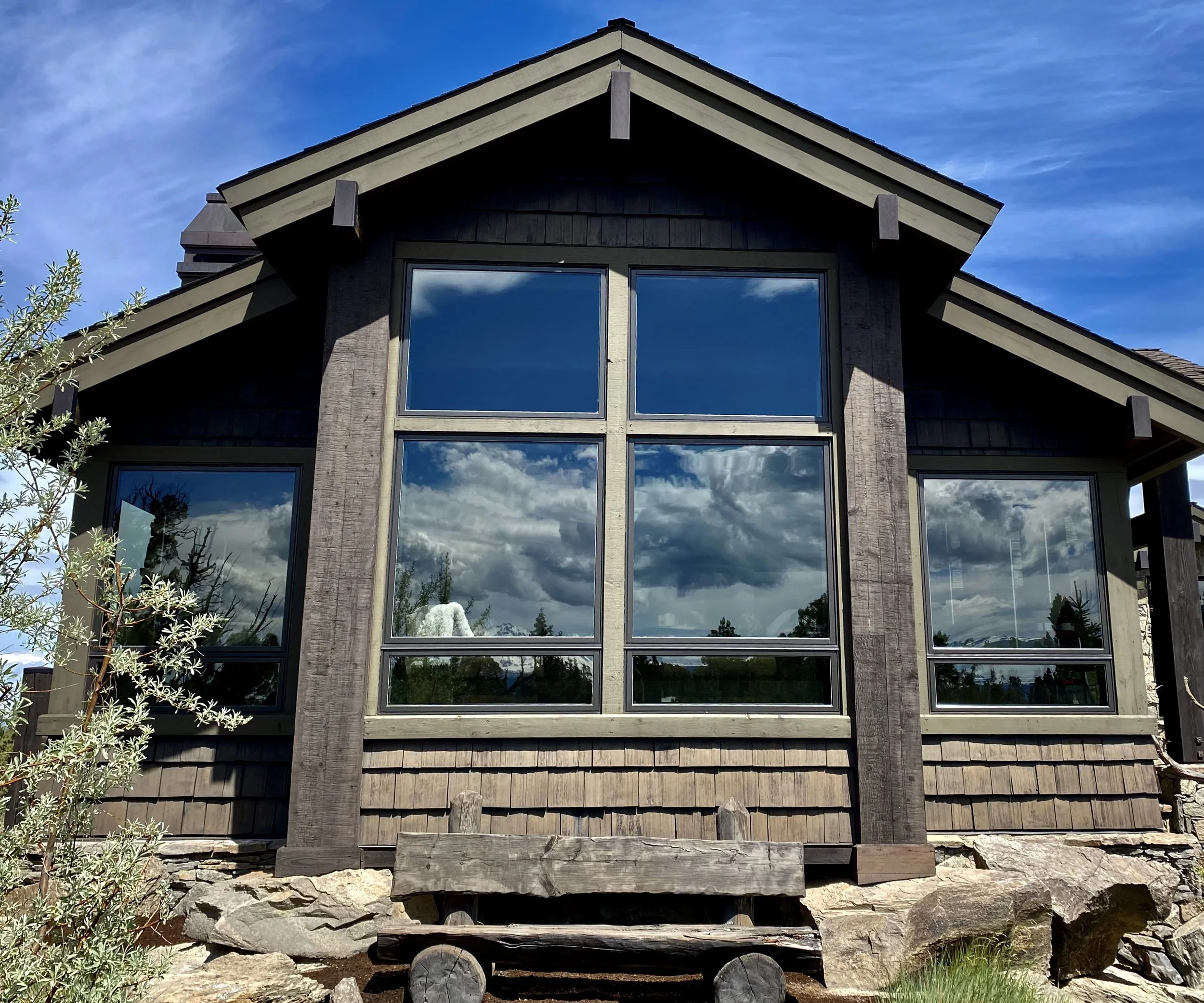 Front view of a house with large glass windows and a gabled roof, reflecting a cloudy sky.
