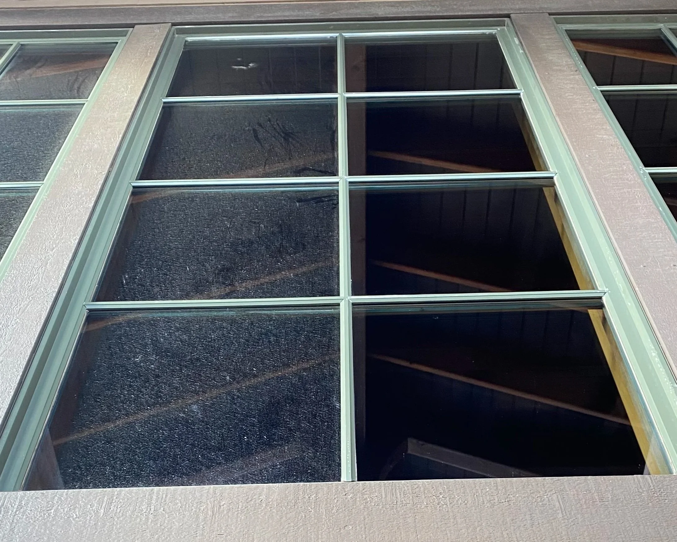 Close-up of a large glass window with multiple panes, framed by green metal, part of a building's exterior wall.