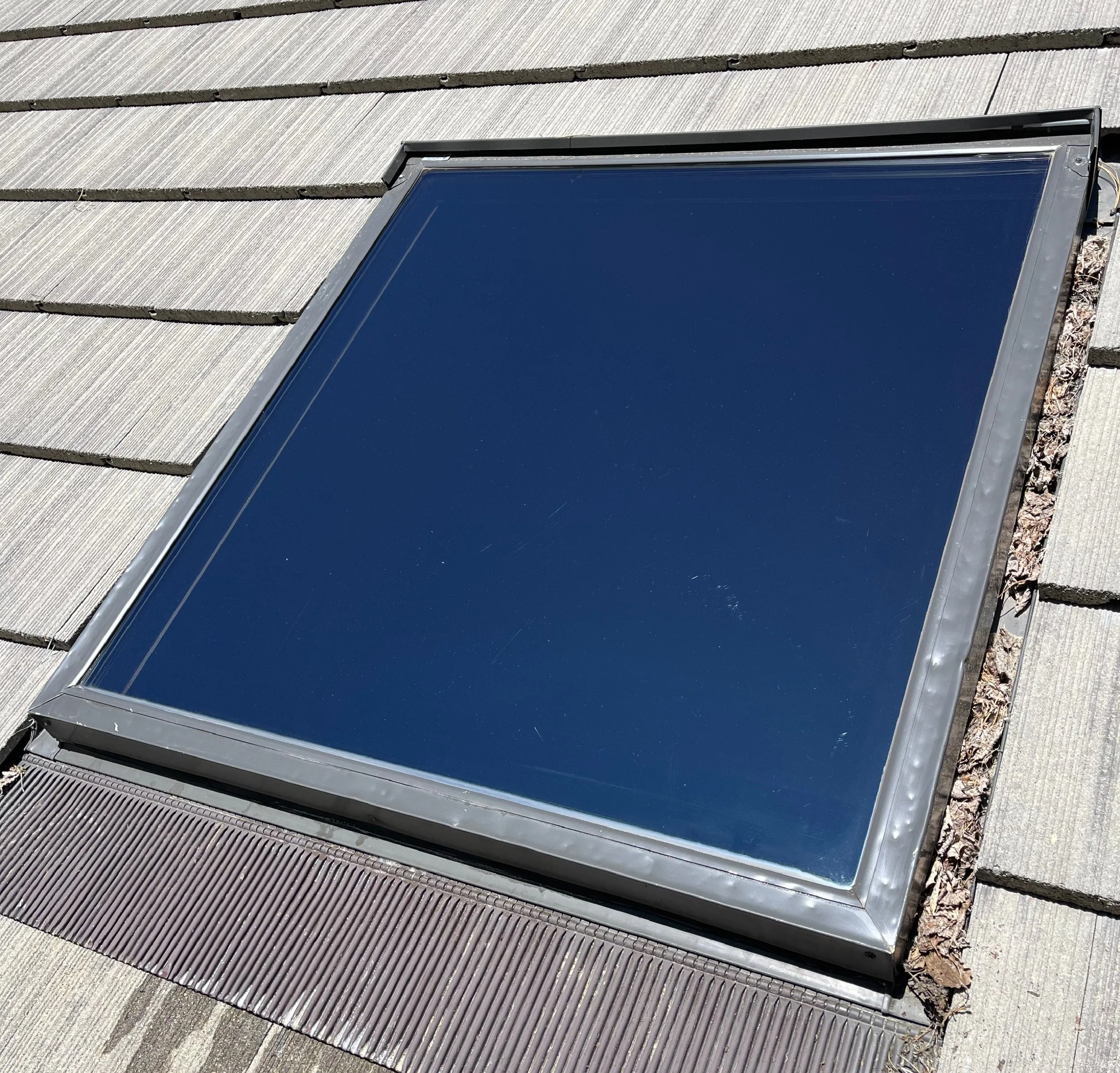 A clean window installed on a sloped rooftop with gray shingles and a copper-colored vent at the bottom.