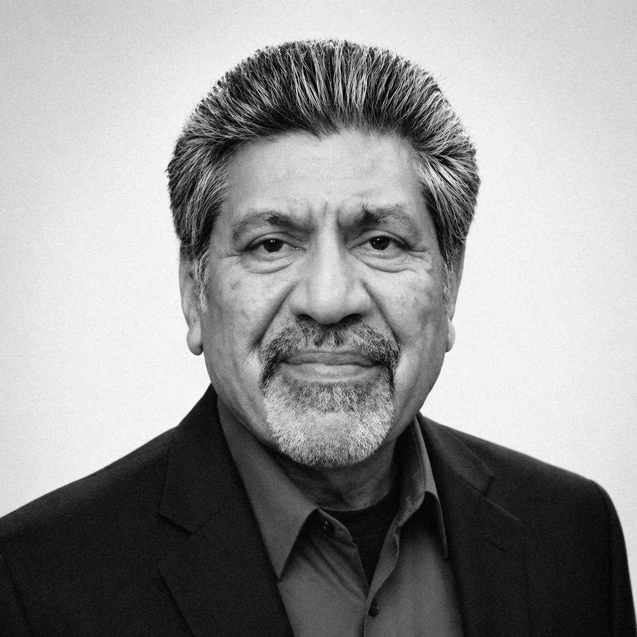 Black and white portrait of Navnit Bhalla with gray hair, beard, and mustache, wearing a dark suit jacket and shirt, looking directly at the camera with a neutral expression.