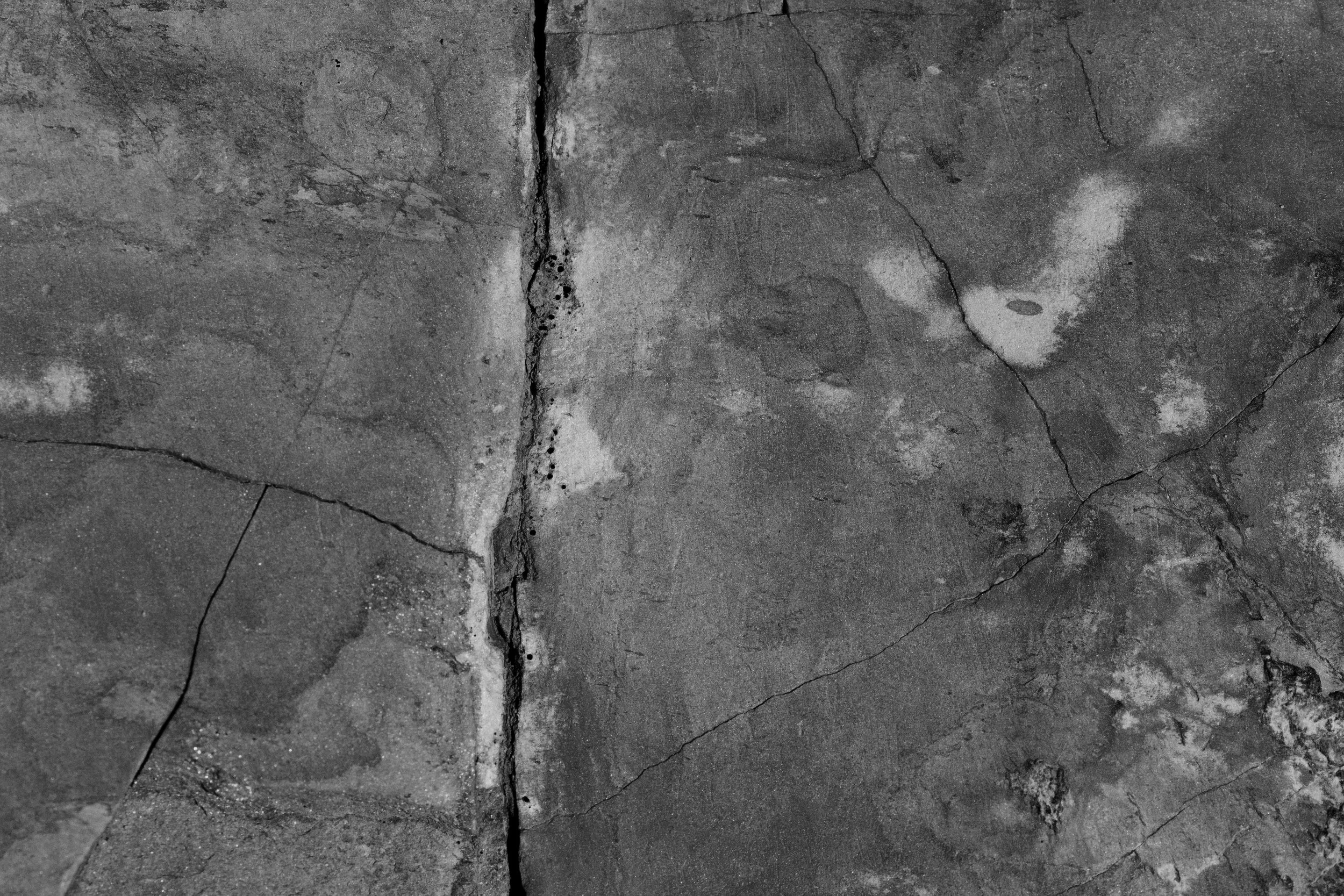 Close-up of worn and cracked concrete floor with various marks, stains, and scratches.
