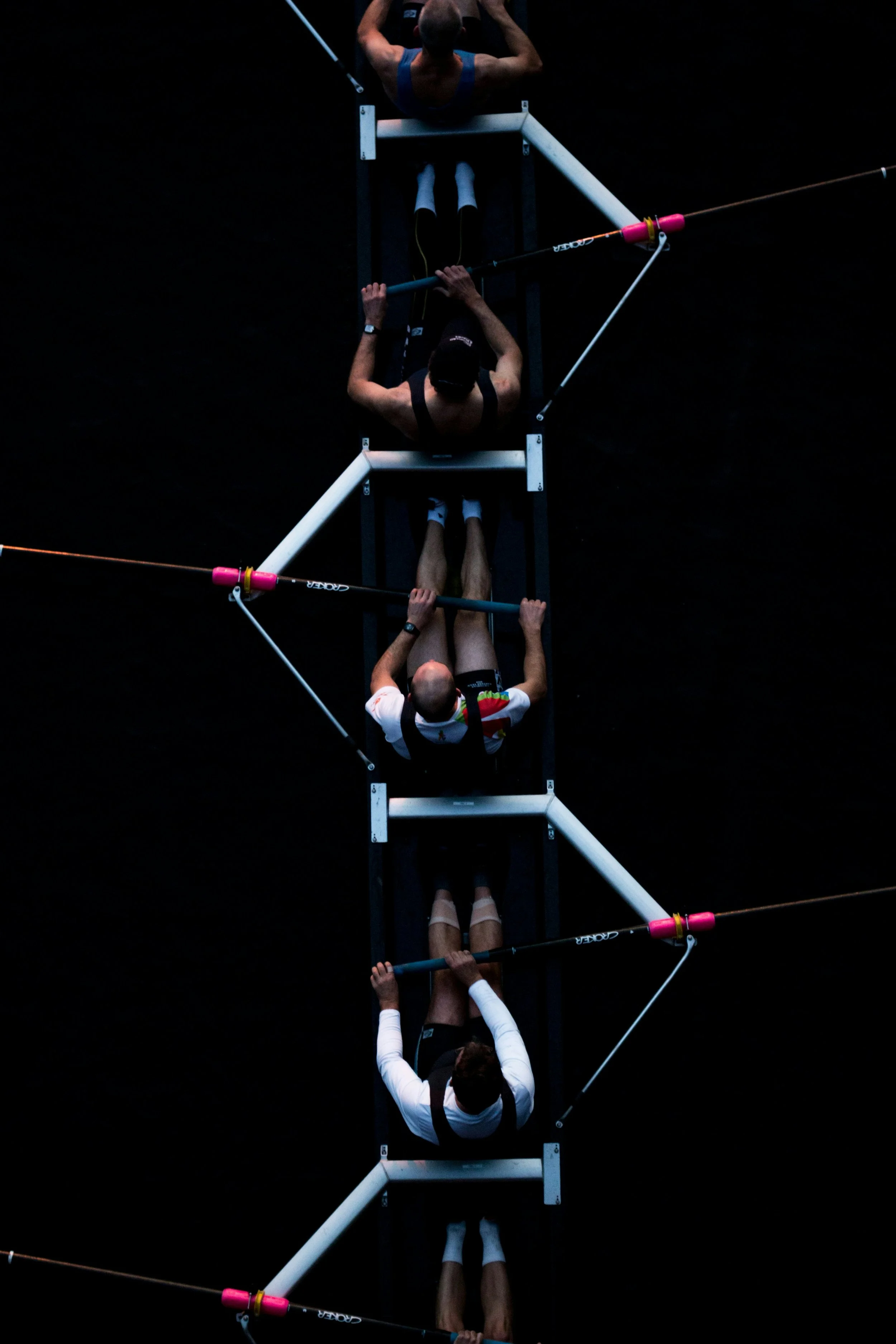 Overhead view of four rowers sitting in a boat, preparing to row, with dark water surrounding them.