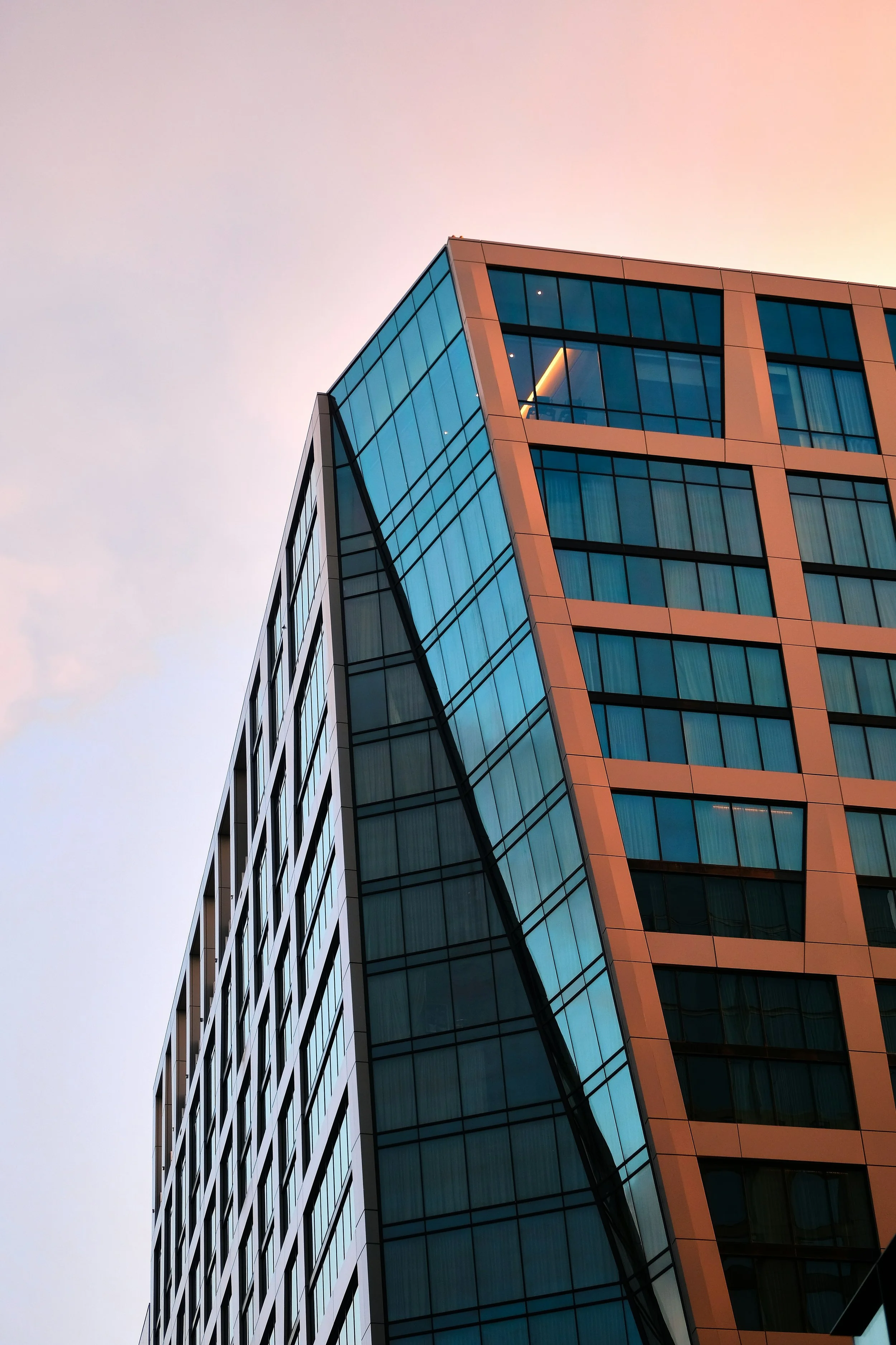 Close-up view of a modern glass office building during sunset, showing clean architectural lines and reflective windows.