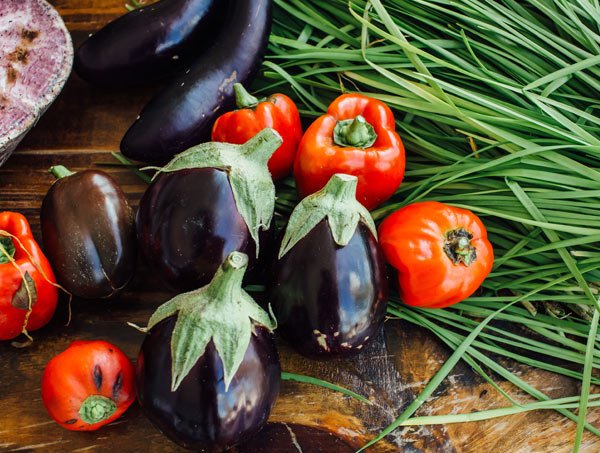 Fresh eggplants, red tomatoes, and green chives on a wooden surface.