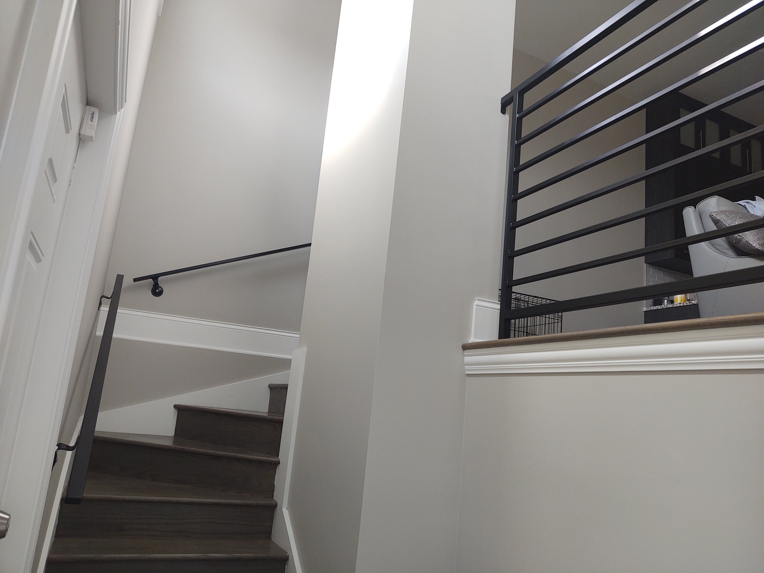Interior view of a staircase with wooden steps, black metal handrails, and white walls in a modern home.