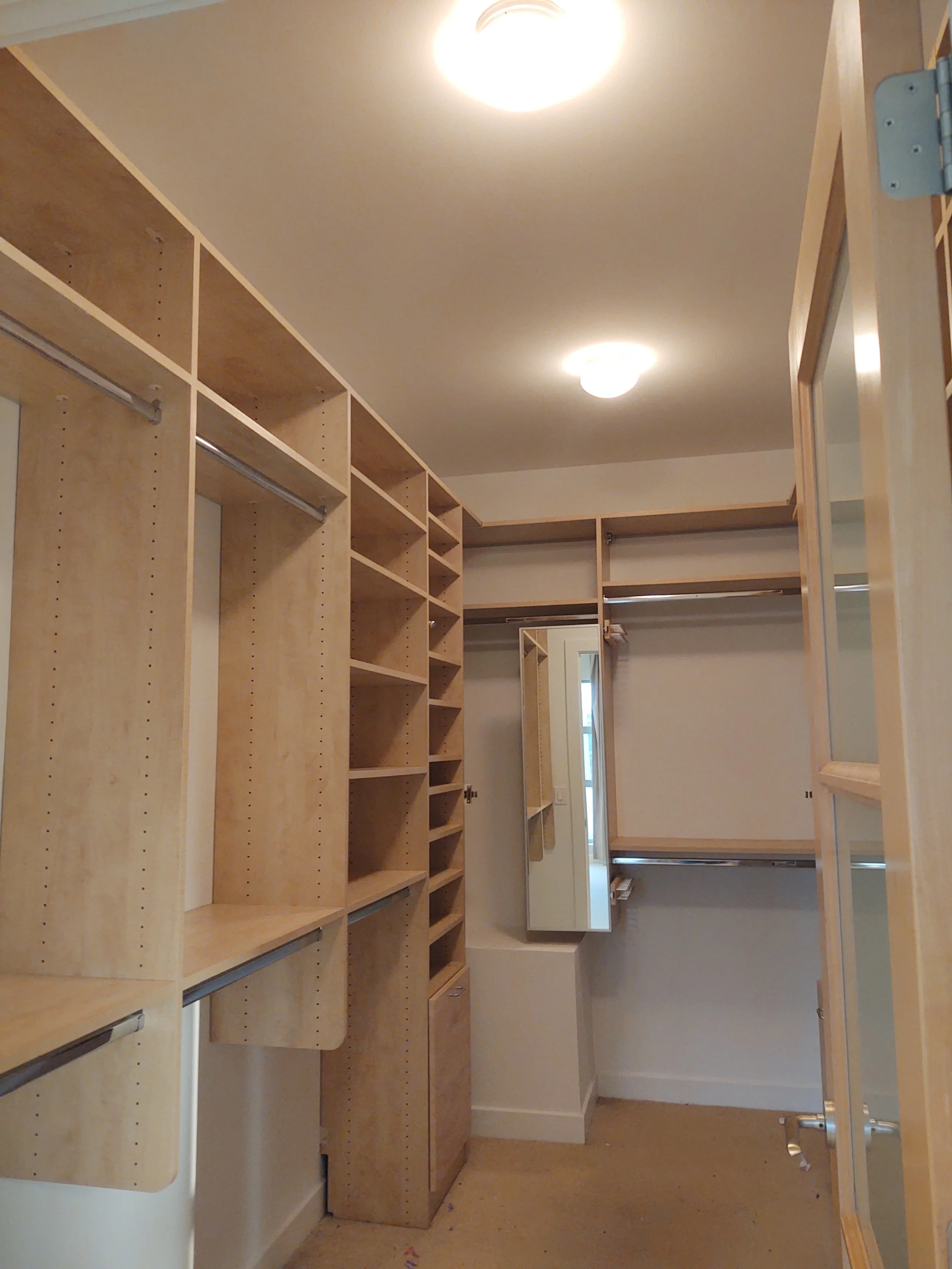 Empty walk-in closet with wooden shelving and hanging rods, illuminated by ceiling lights.