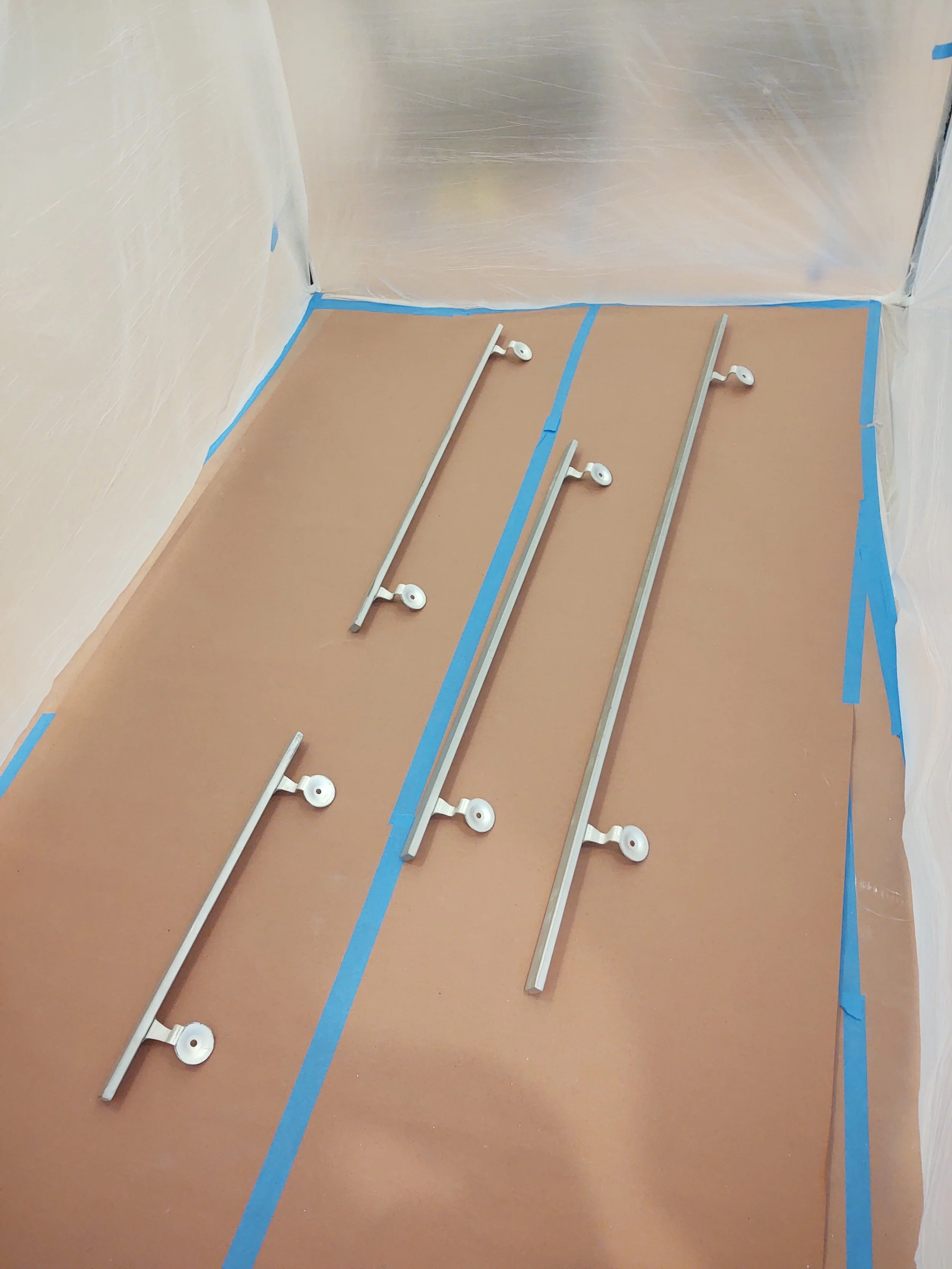Bathroom with metal grab bars installed on the floor, with blue painter's tape along the edges of the walls and floor, and plastic sheeting covering the walls.