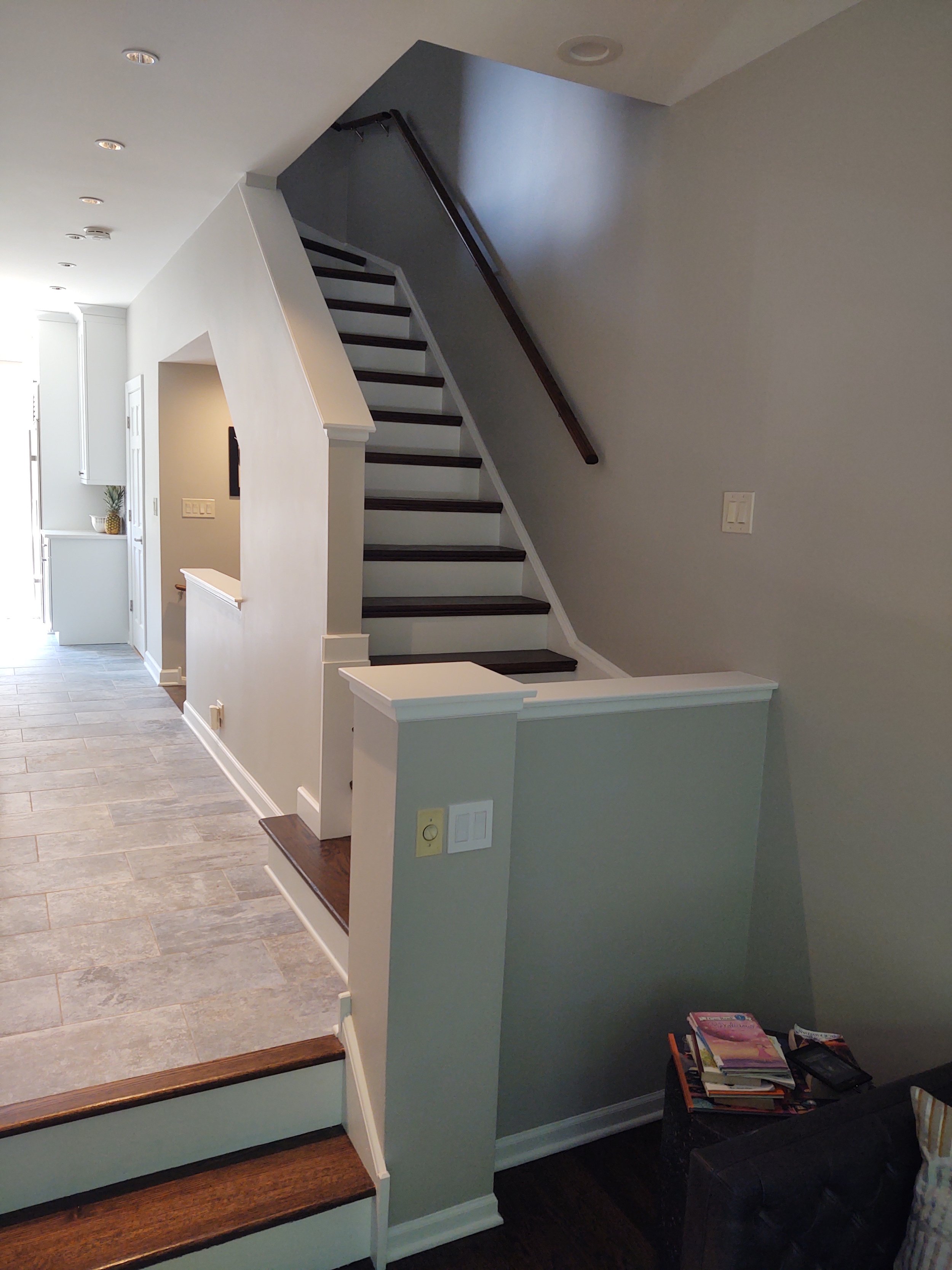 Interior of a home showing stairs with dark wooden steps and white risers, a small landing area, beige walls, and a hallway leading to another part of the house.