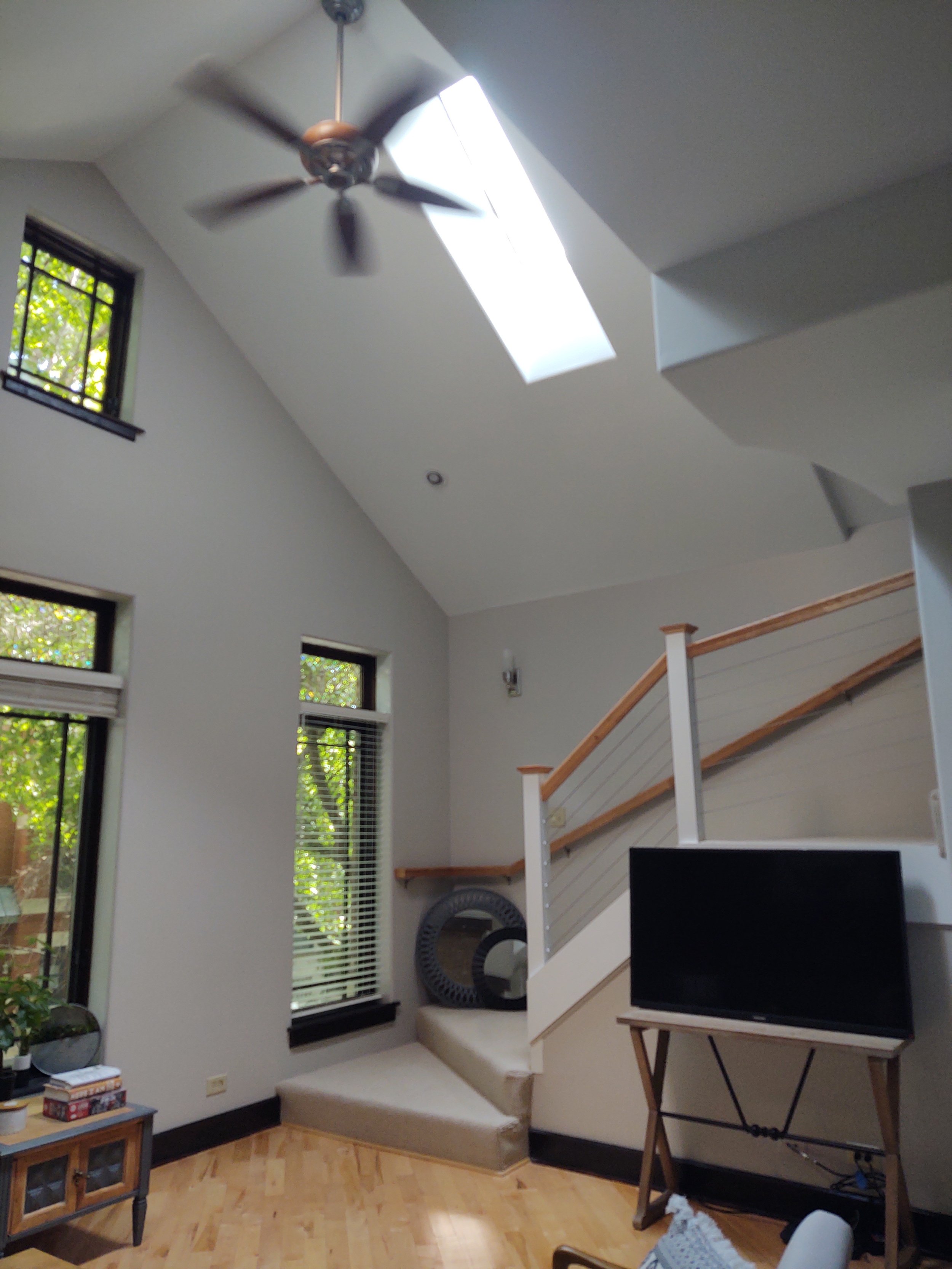 Living room with high ceiling, skylight, ceiling fan, and windows, with furniture and decor.
