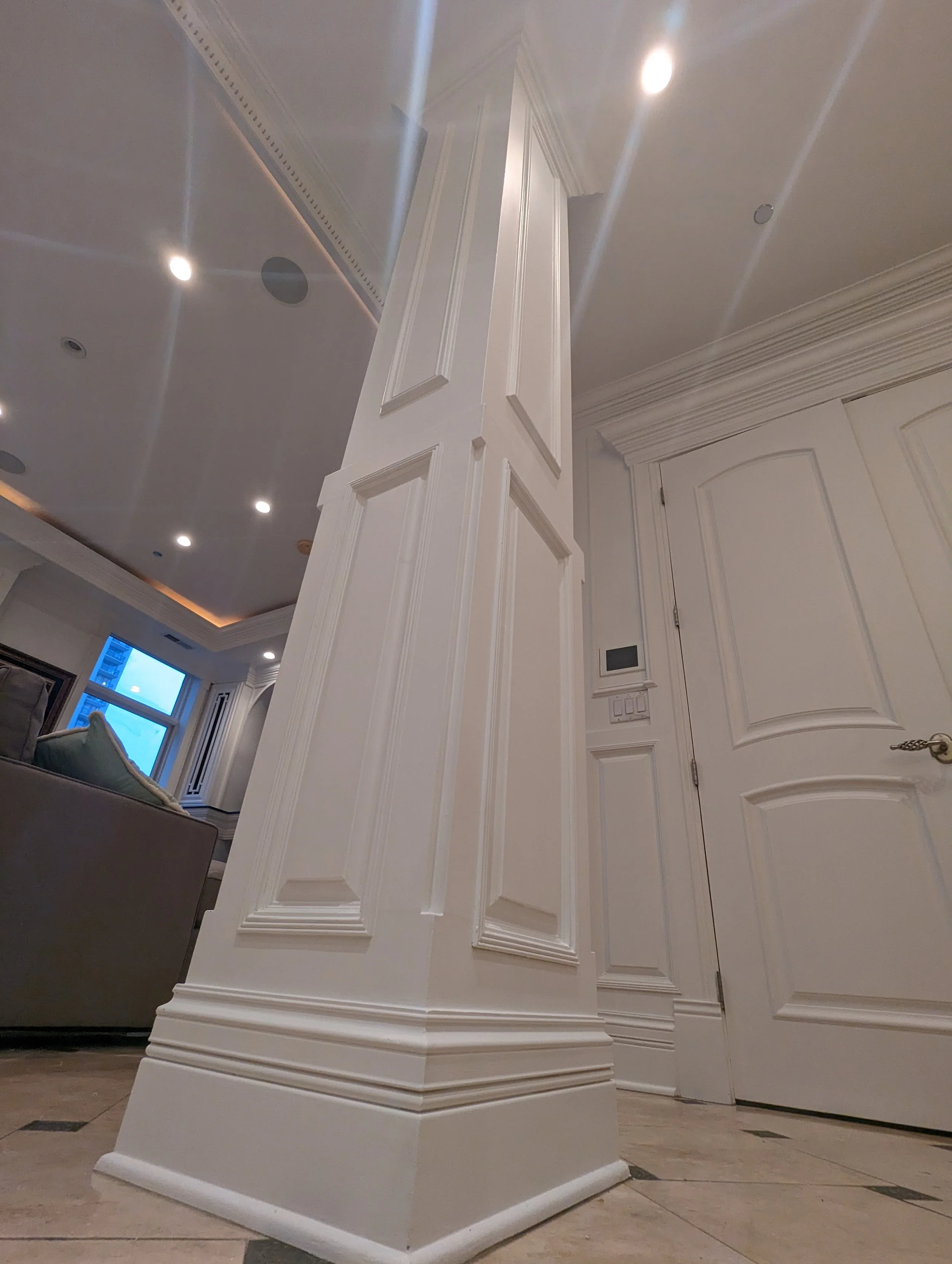 Interior view of a room corner with decorative white wood molding, a door, and ceiling lights.