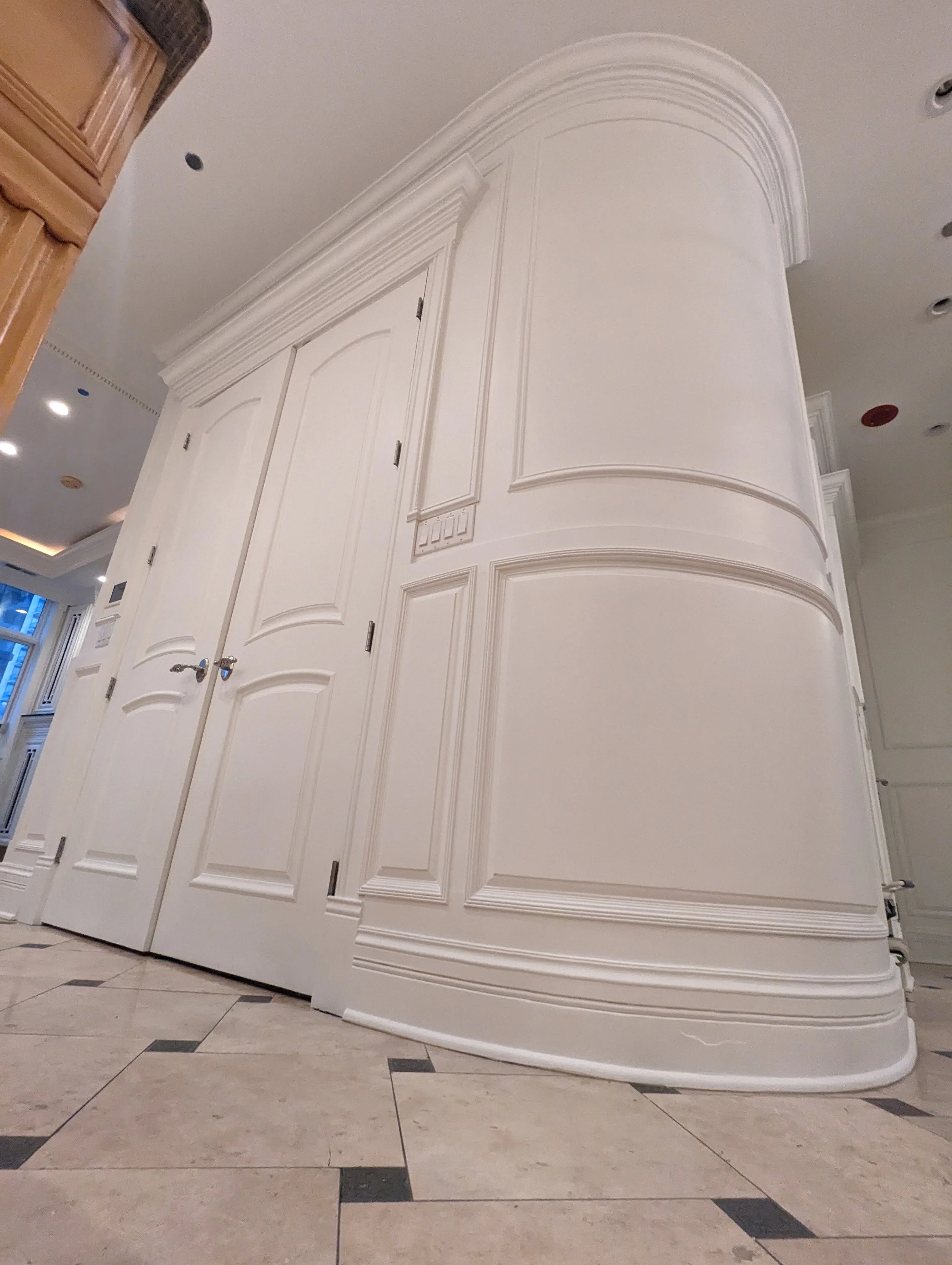 White ornate wall with detailed molding and double doors in an interior space with tiled floor.
