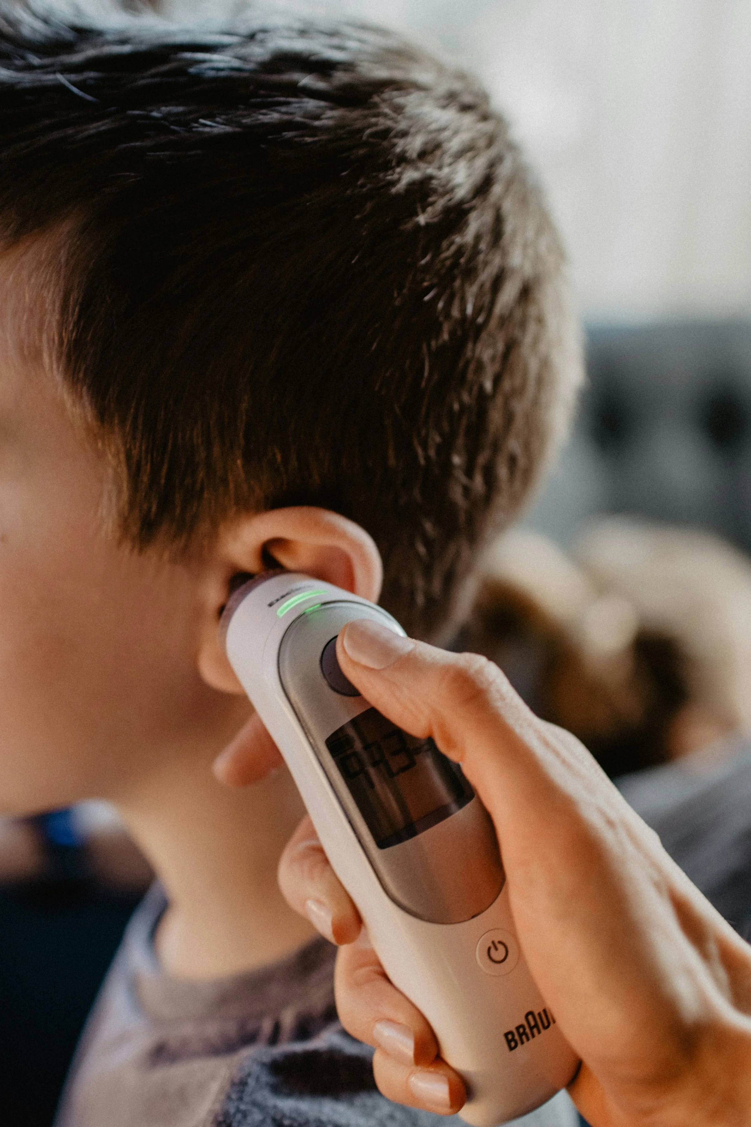 A person using a digital ear thermometer to measure a child's ear temperature.