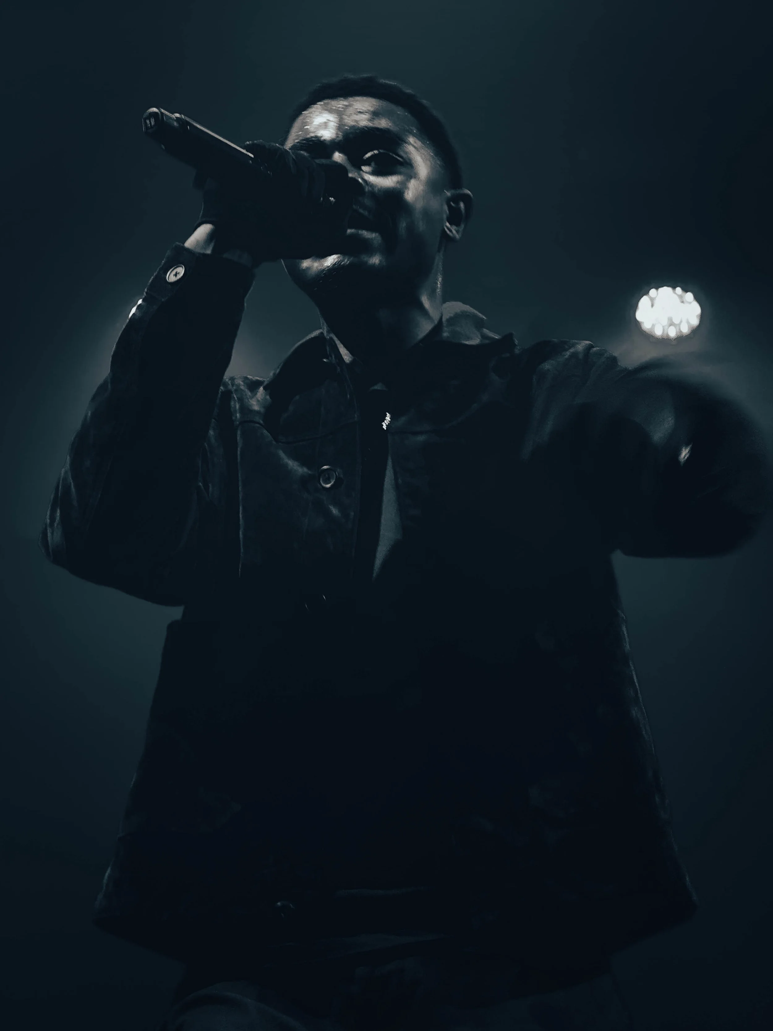 A male singer performing on stage, holding a microphone close to his face, under dark stage lighting.