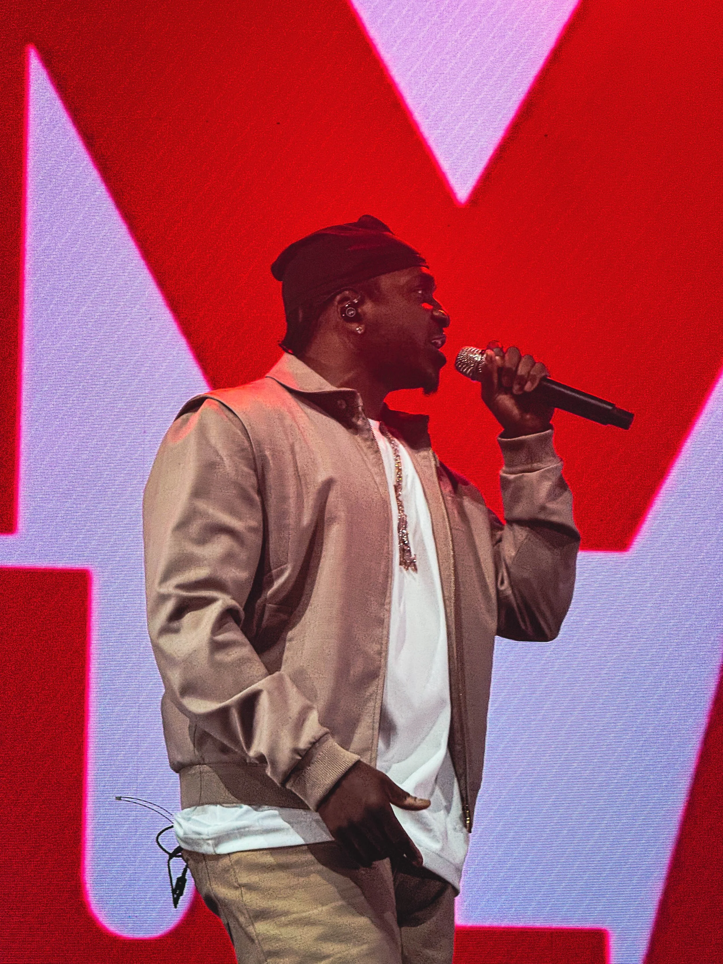 Man holding microphone on stage in front of red promotional backdrop.