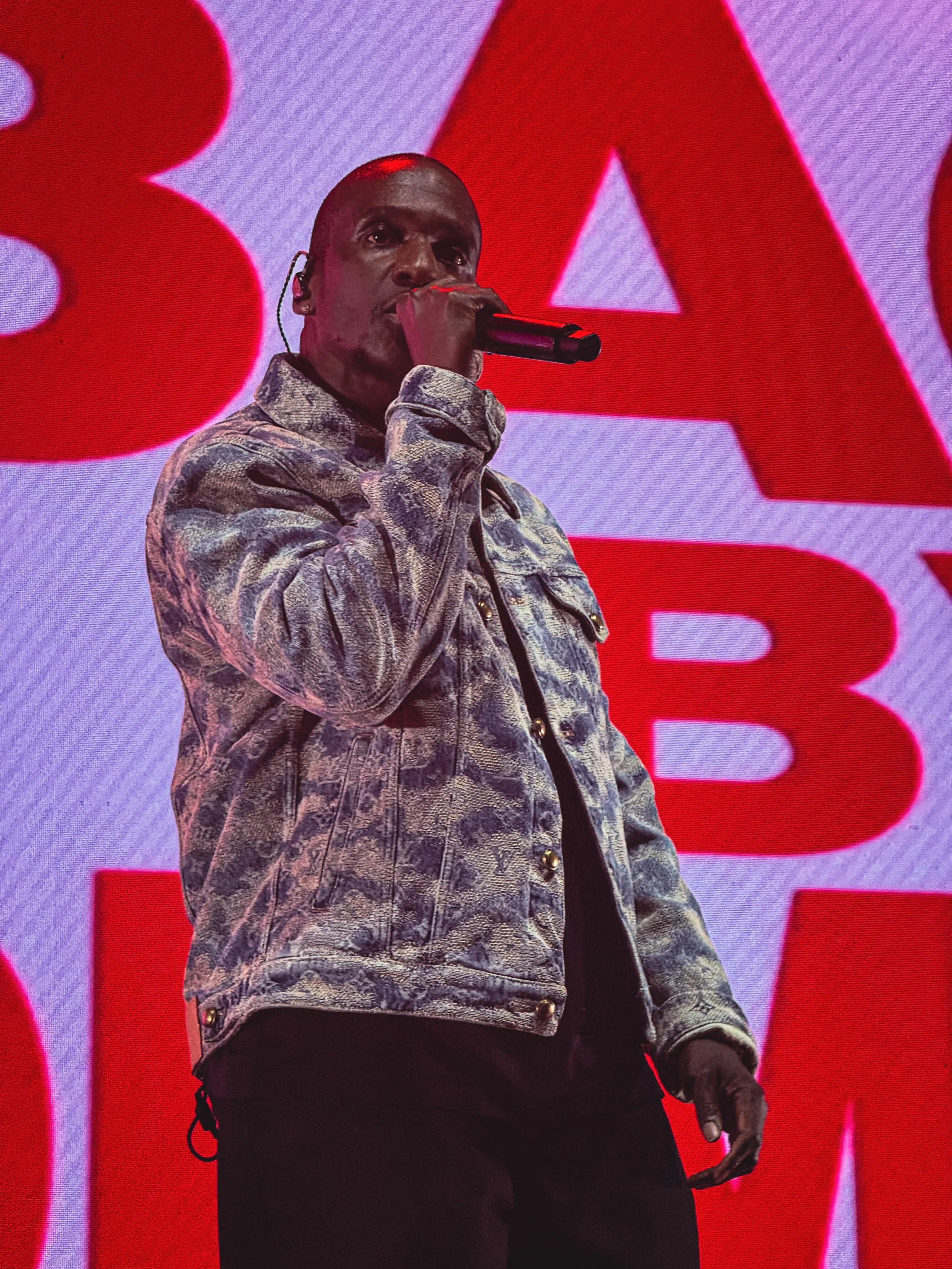 A man holding a microphone on stage in front of a large LED screen displaying the words 'BLACK' in red capital letters.