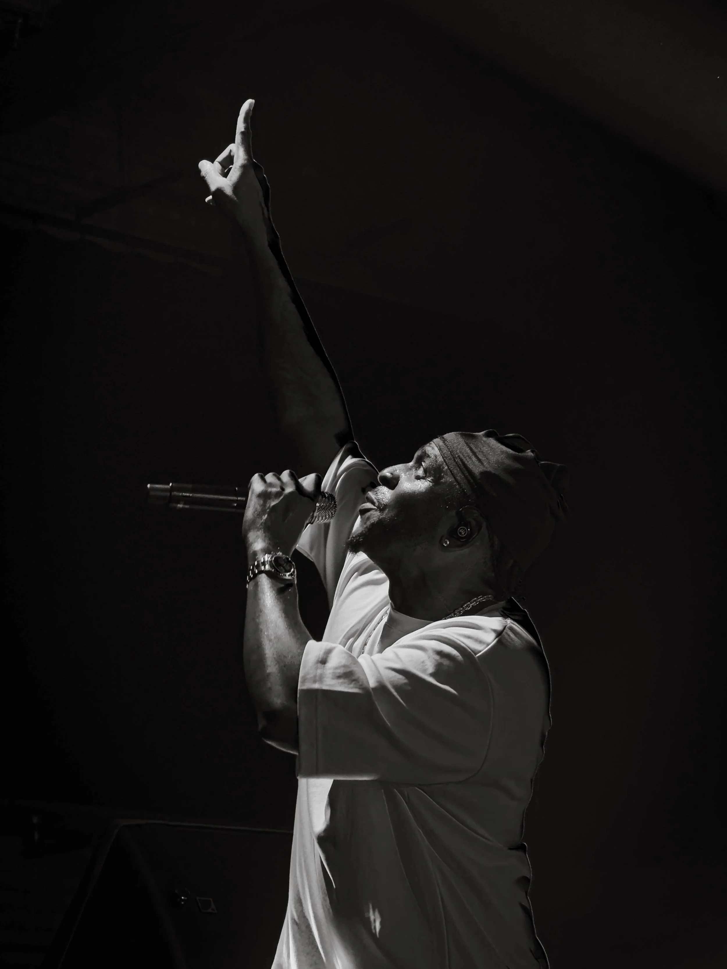 A singer passionately performing on stage, with one arm raised, holding a microphone, and wearing a head covering.
