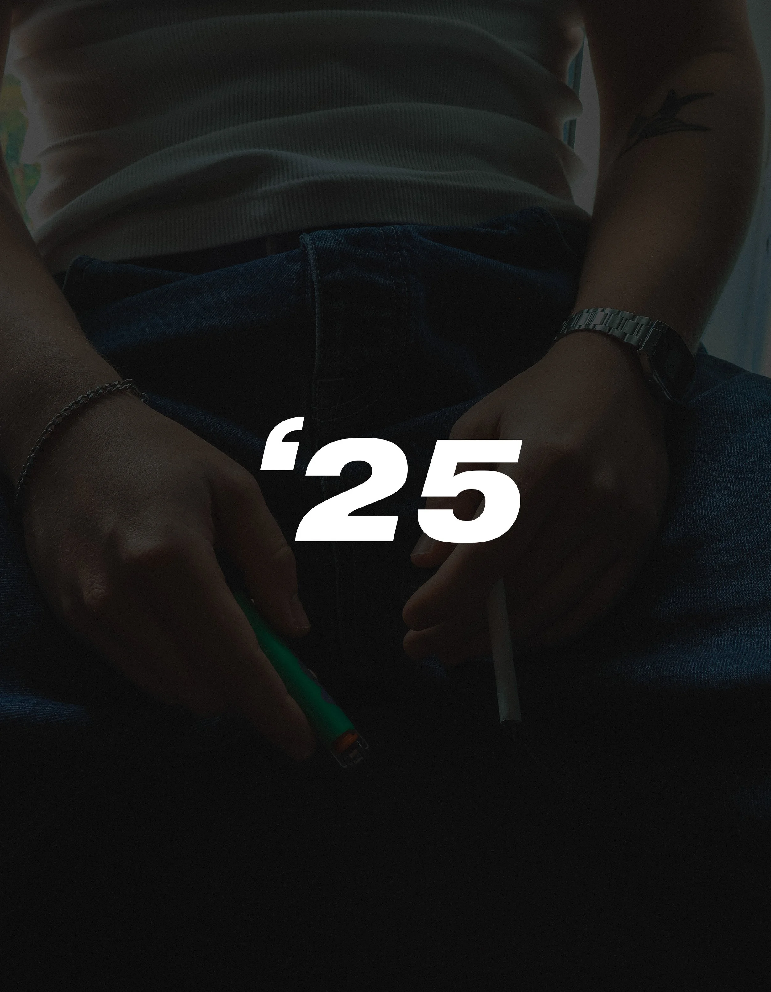 Person sitting down wearing a white shirt, blue jeans, a silver watch, and a bracelet, holding a green lighter and a cigarette with the number 25 overlaid on the image.