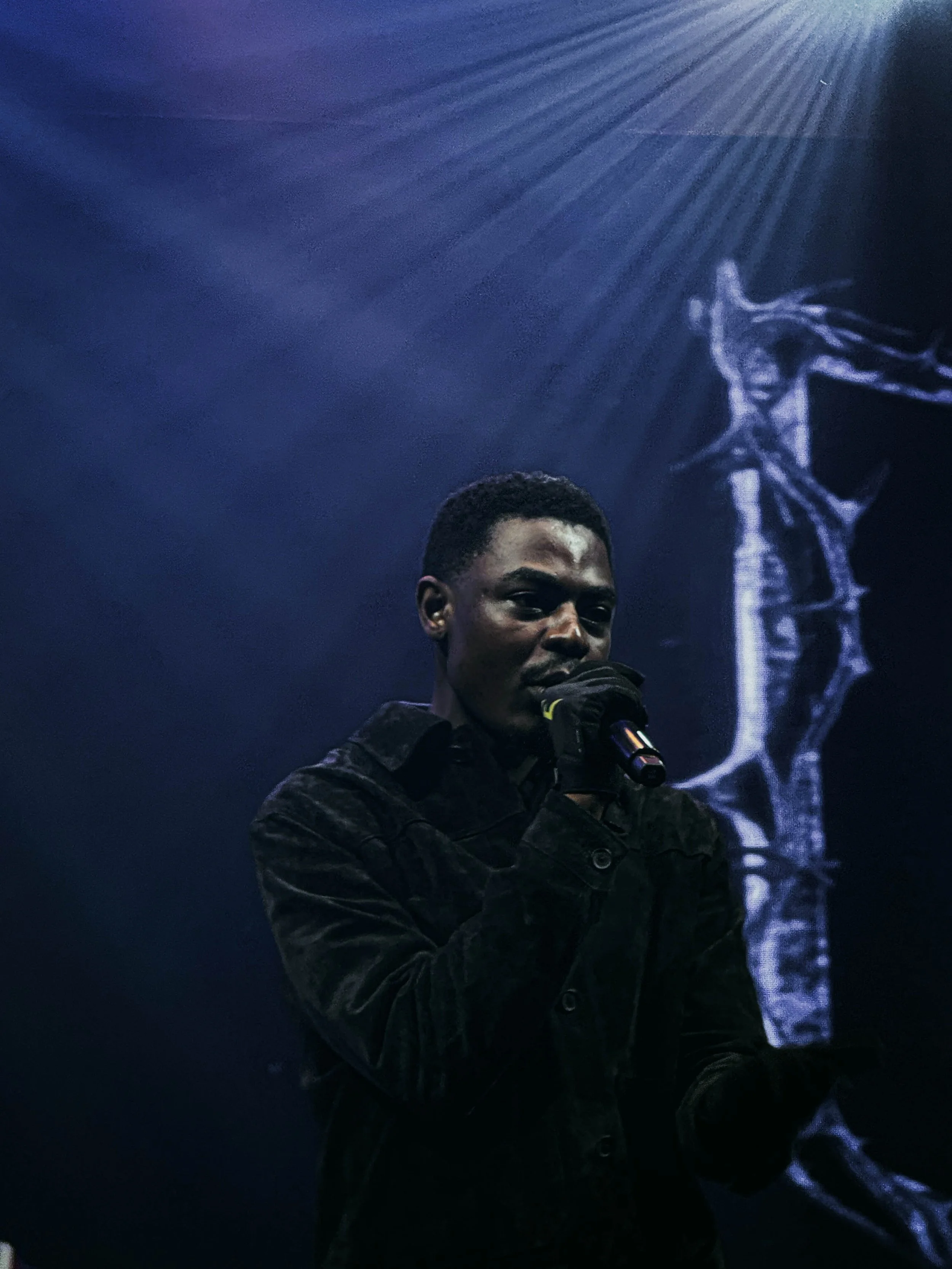 A person holding a microphone on stage with a dark background and a skeleton projection.