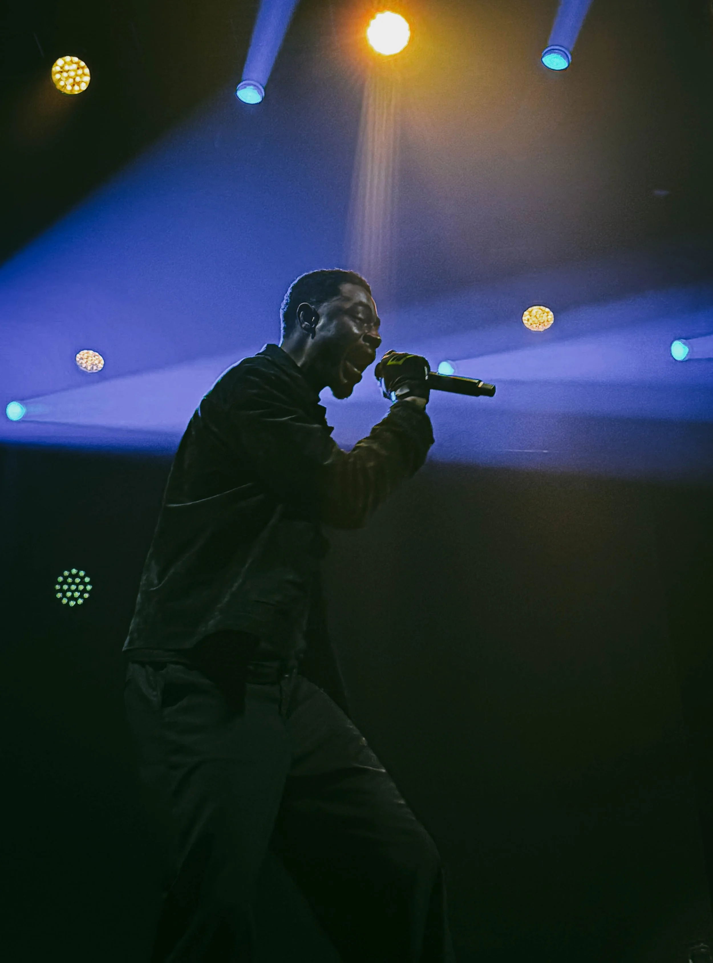 A male singer performing on stage with colorful lights and fog effects.