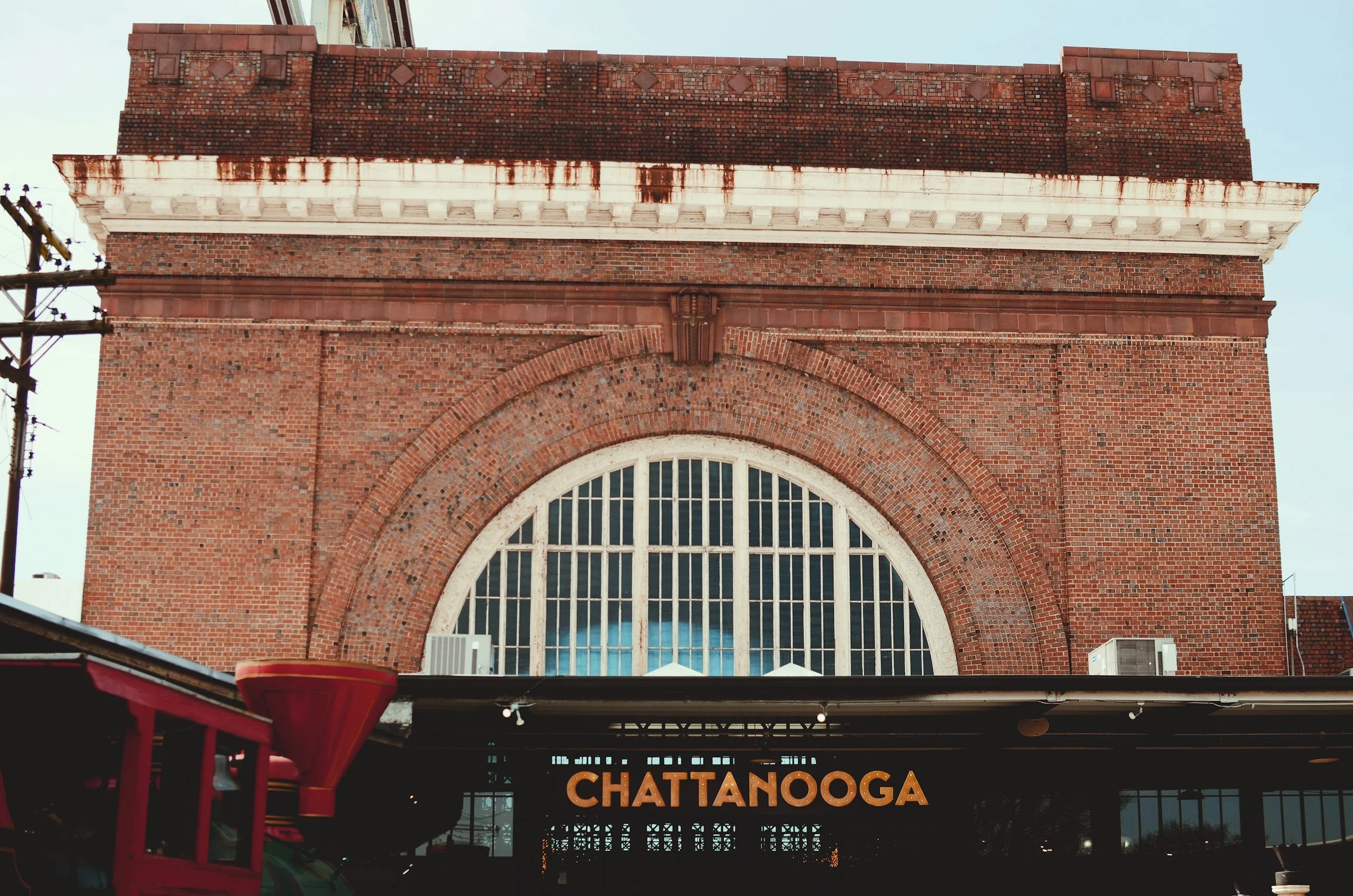 A historic brick building with a large arched window and decorative brickwork, featuring the word '.CHATTANOOGA' in illuminated letters.