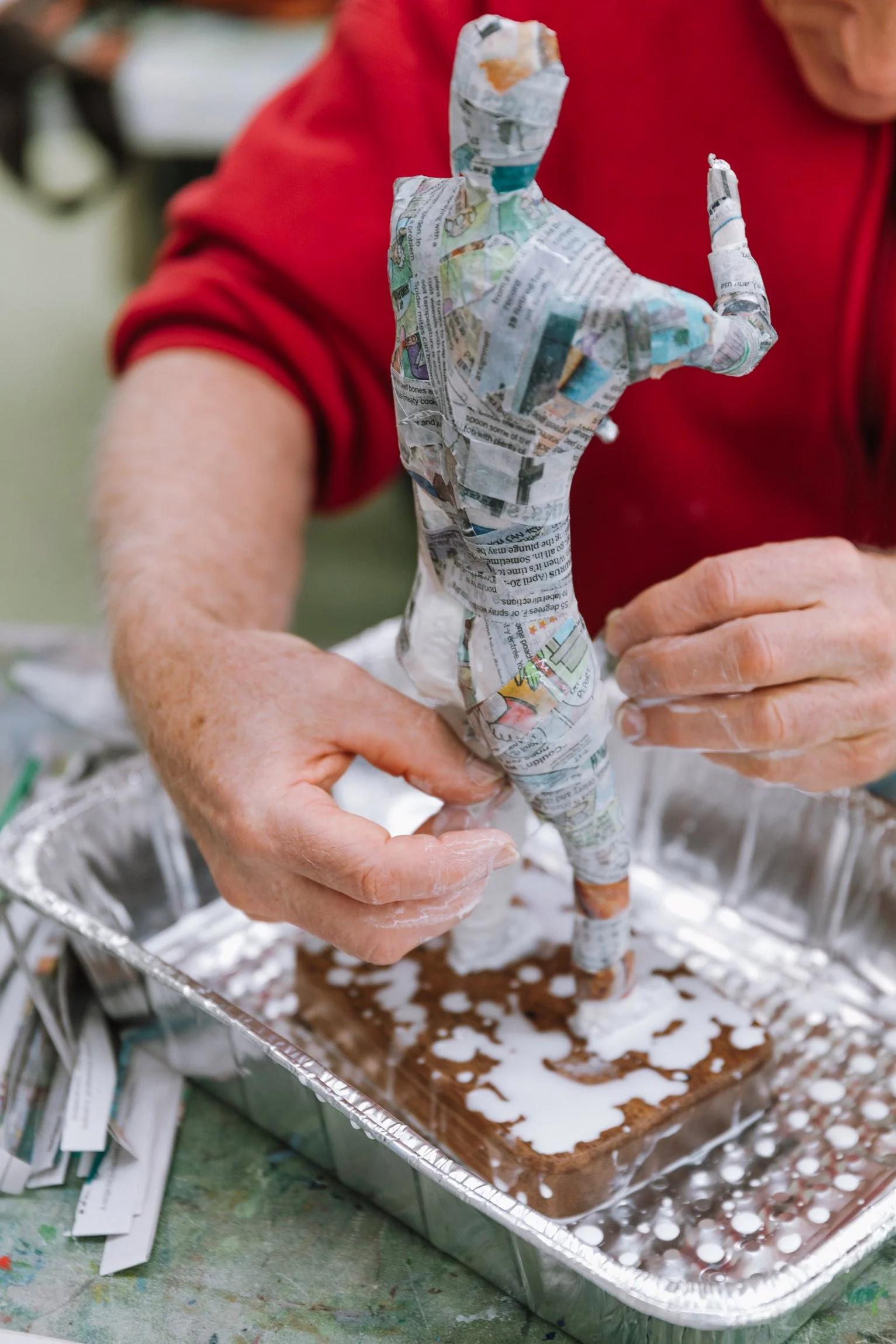 A person wrapping a handmade sculpture of a dog in newspaper, making it appear lifelike. The scene suggests a craft or art project.