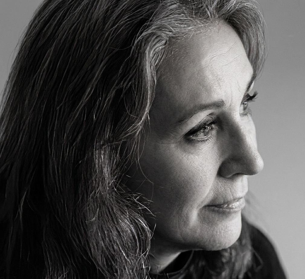 Black and white close-up of a woman with long, wavy hair, looking to the right with a gentle expression.
