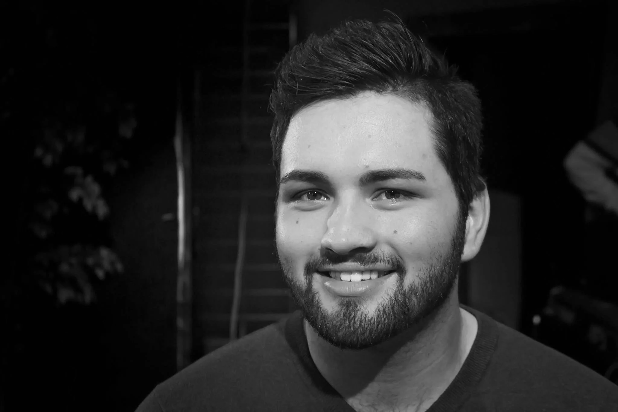 Black and white photograph of a young man with short dark hair and a beard, smiling and looking at the camera.