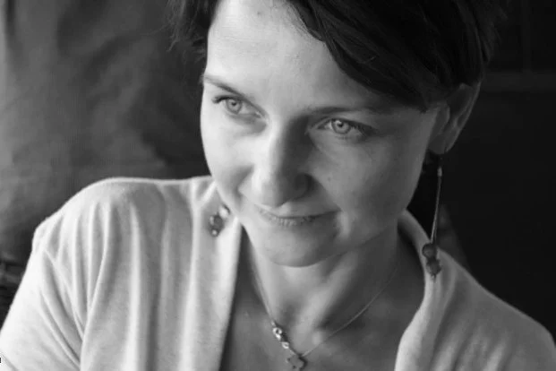 Black and white photo of a woman with short dark hair, wearing earrings and a necklace, looking to her left with a slight smile.