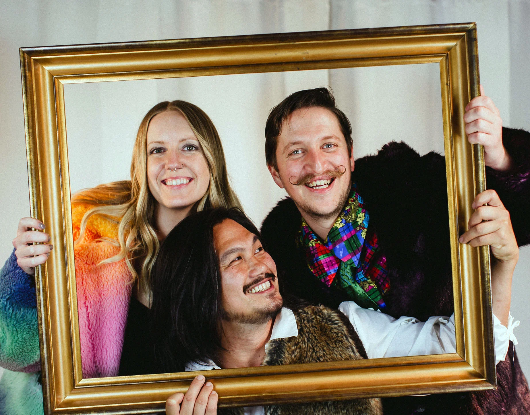 Three people smiling and looking through a gold picture frame.