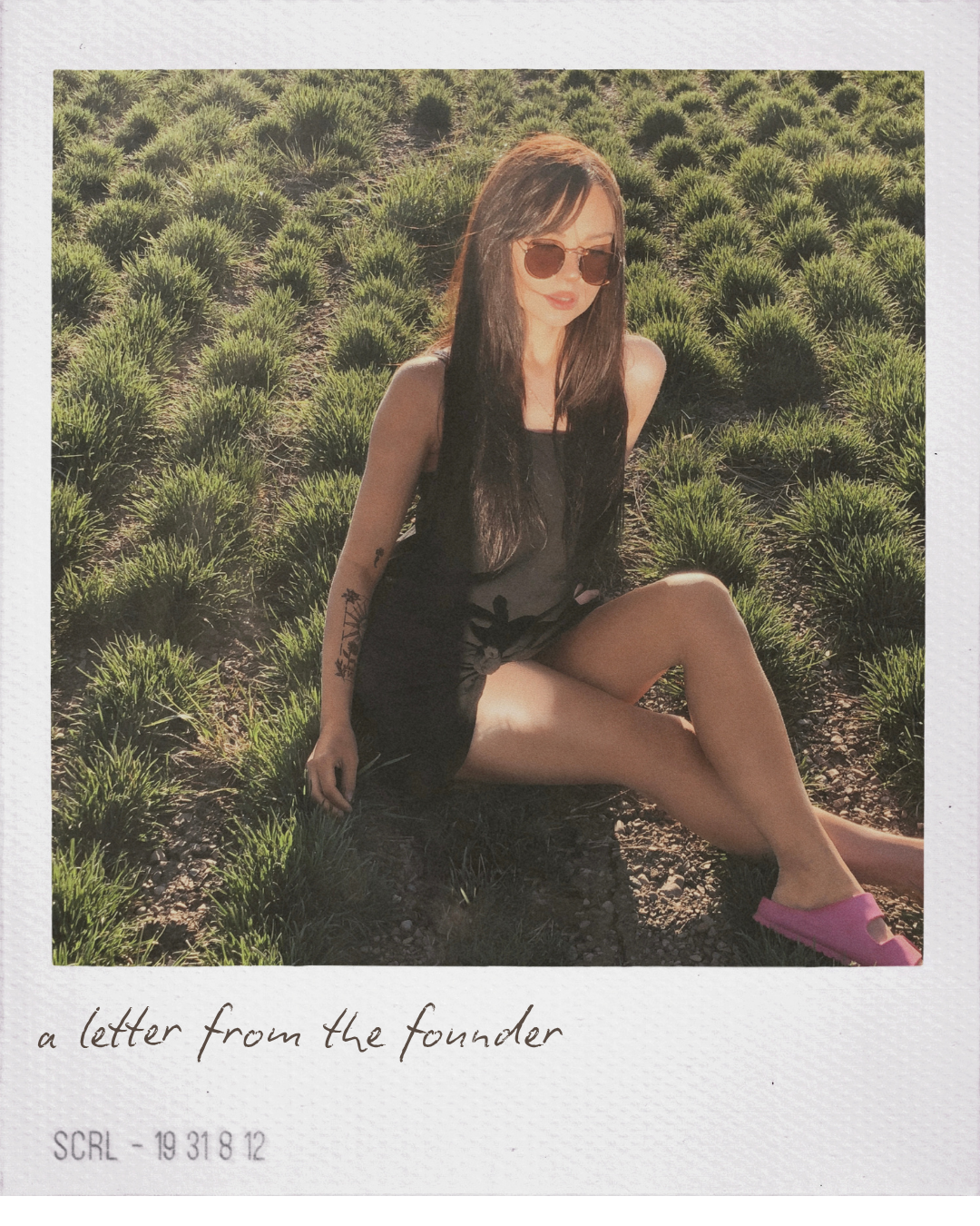 Tyler, founder of Apothek Interest, sitting outdoors in a grassy field wearing sunglasses. A polaroid-style film photo for the small-batch, non-toxic beauty brand.