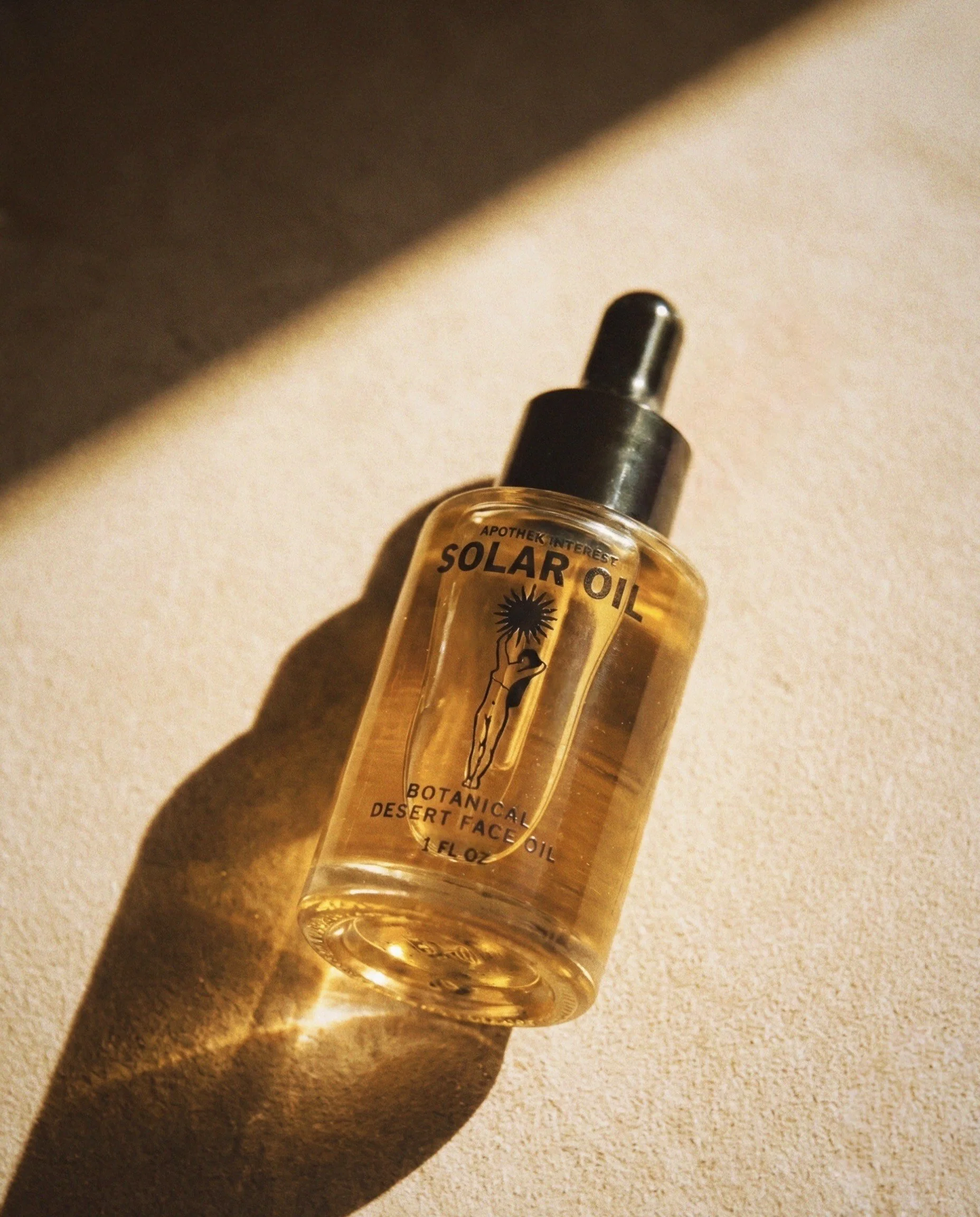 Apothek Interest Solar Face Oil 1 oz dropper bottle resting on warm stone. Golden sunlight illuminates the botanical desert serum, casting a deep shadow over the minimalist label.