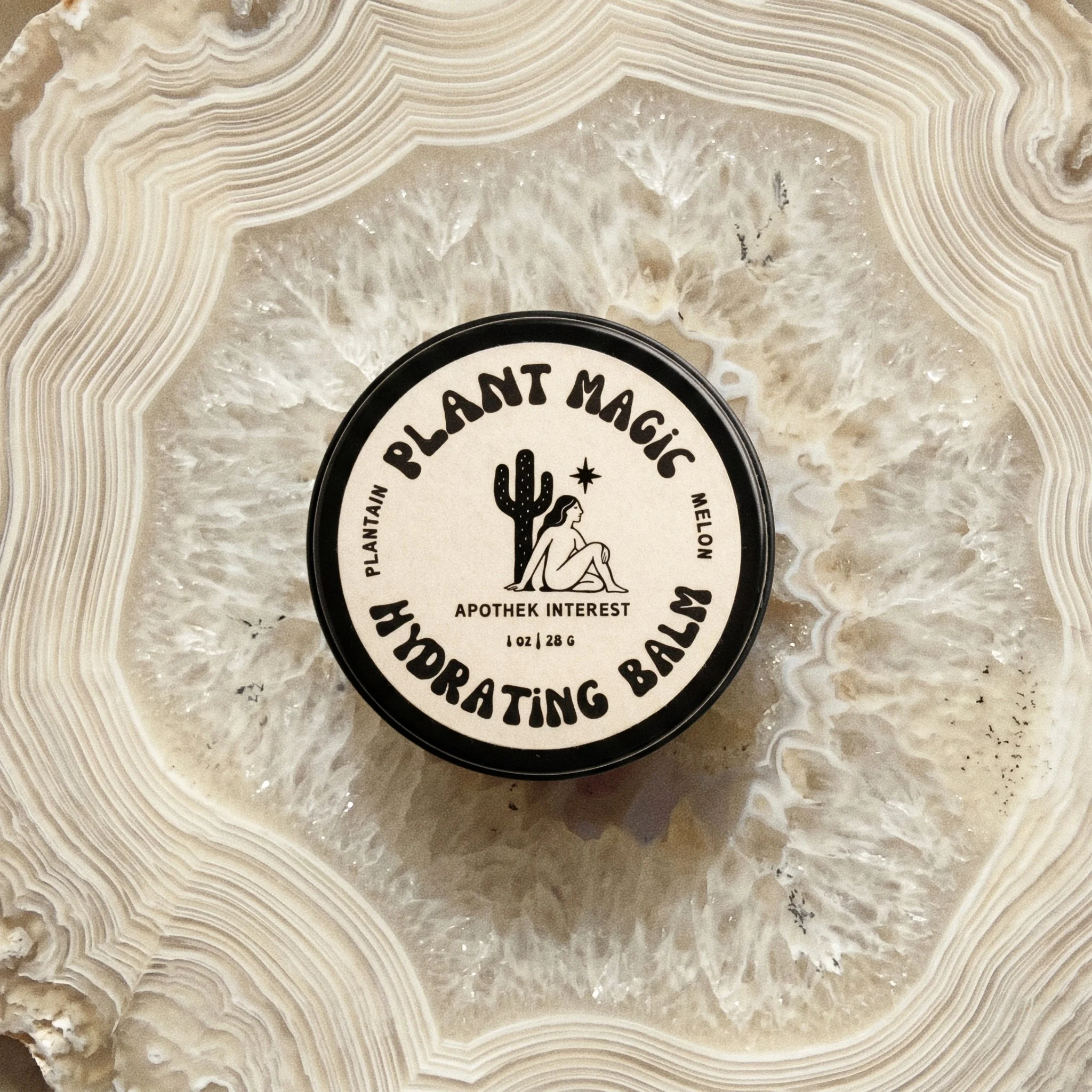 Top-down view of Apothek Interest Plant Magic Hydrating Balm tin resting on a slice of crystalline agate stone.