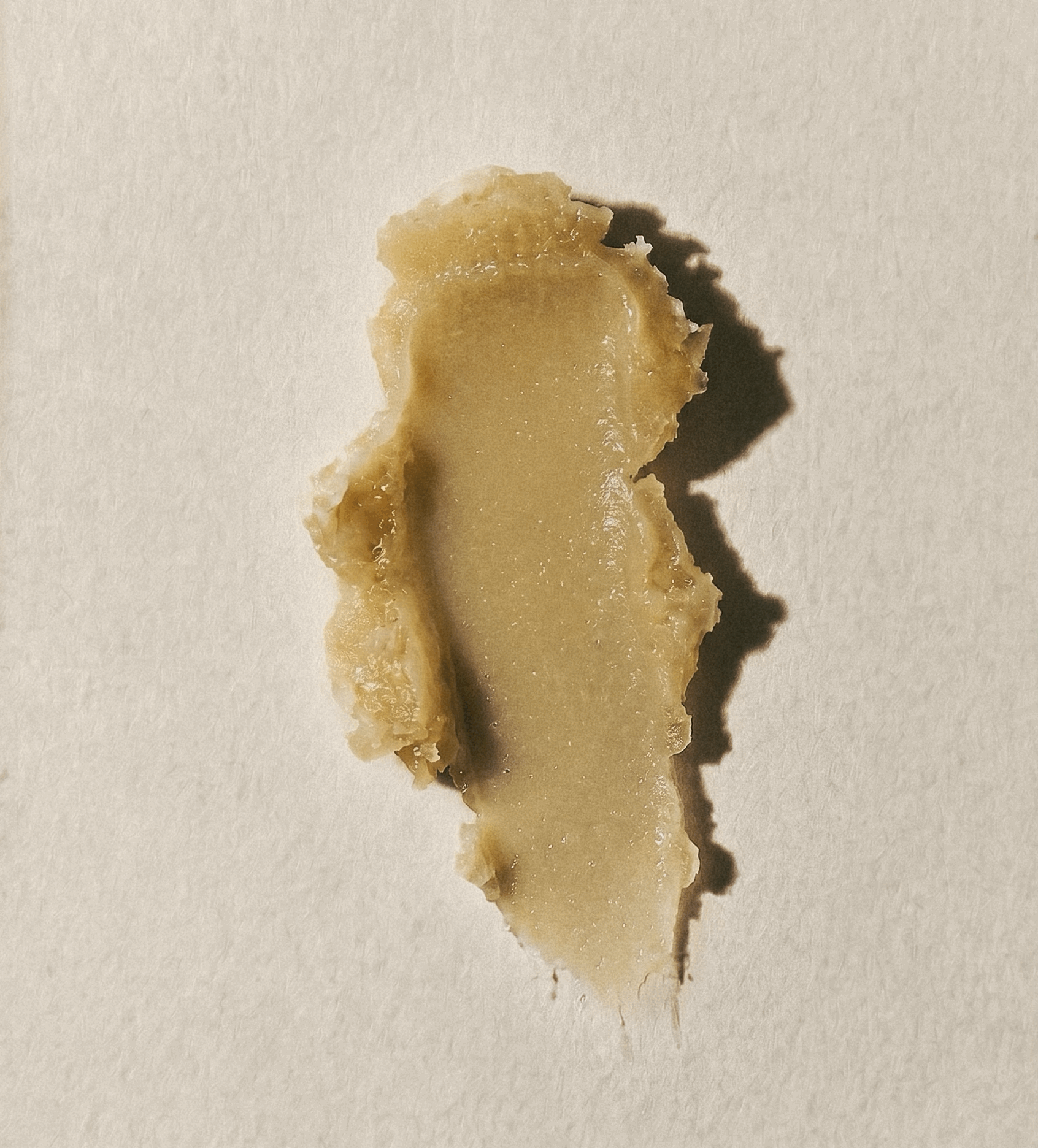 A close-up texture swatch of Apothek Interest's Plant Magic Hydrating Balm. The salve is a smooth, buttery, pale-green color smeared against a cream textured background.