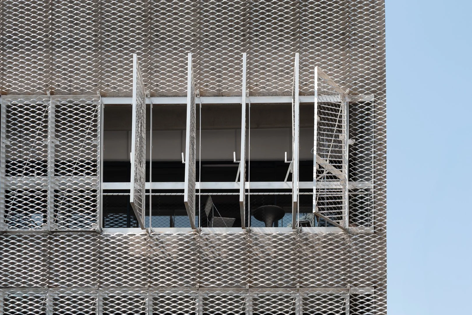 Fachada arquitectónica con malla metálica desplegada, proyecto desarrollado junto a oficina de arquitectura, solución técnica para control de luz y ventilación.