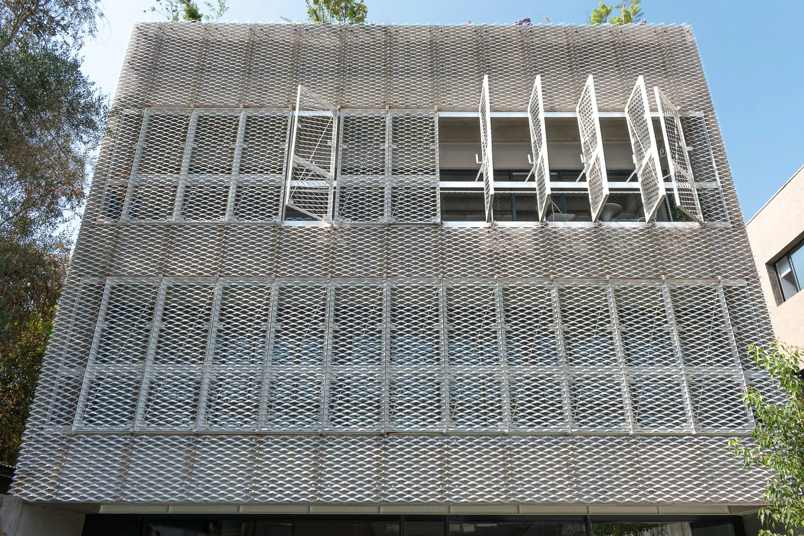 Fachada moderna de un edificio con ventanas y mamparas de protección metálicas en patrones geométricos