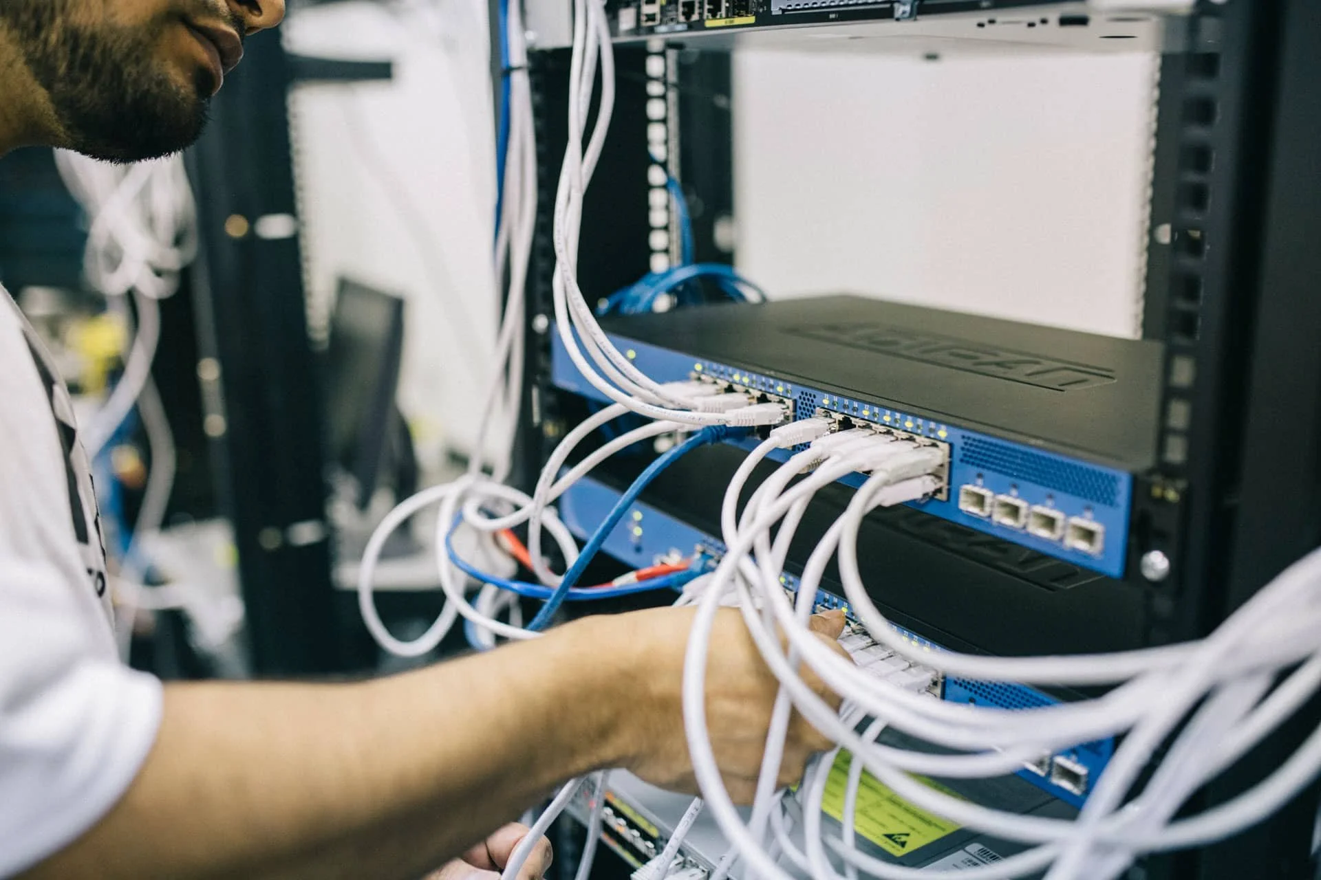 Technician working on a server rack with multiple connected cables and networking equipment.