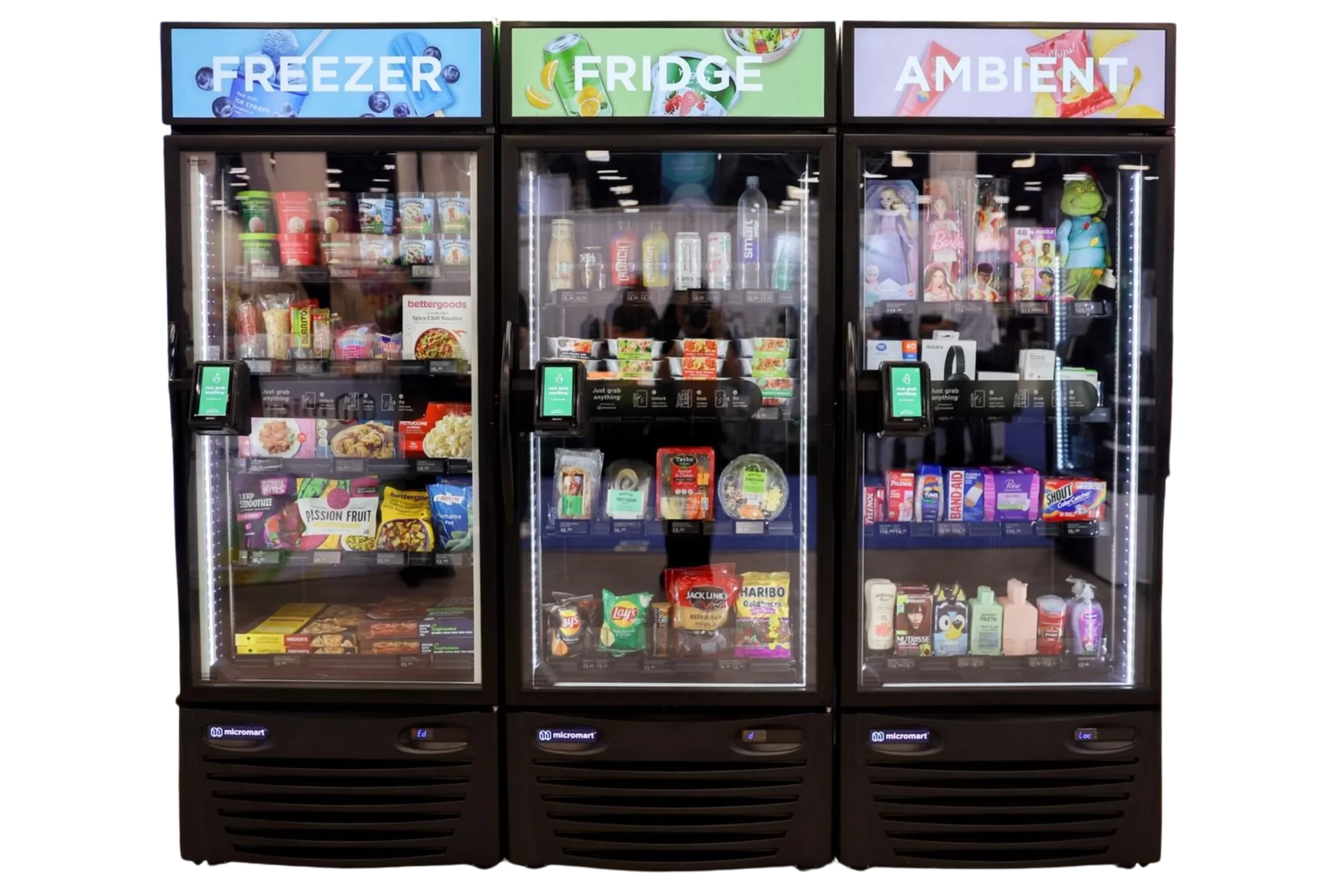 Three glass-front refrigerated vending machines labeled 'FREEZER,' 'FRIDGE,' and 'AMBIENT,' containing snacks, beverages, and frozen foods.