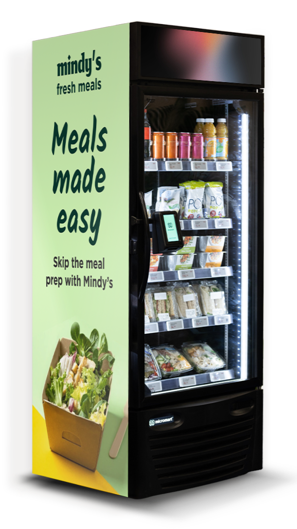 A vending machine with a sign on the side that reads 'Mindy's fresh meals, Meals made easy, Skip the meal prep with Mindy's'. The machine contains bottled drinks, bags of snacks, and pre-packaged meals or salads.