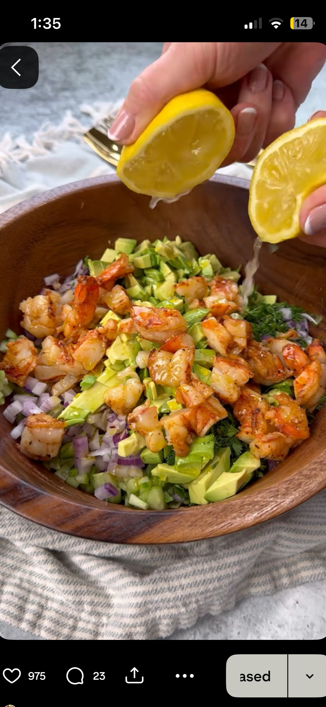 A person squeezing lemon over a bowl of cooked shrimp, chopped avocado, diced onions, and fresh herbs.