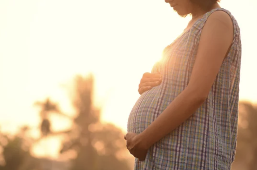 Pregnant woman holding her belly outside during sunset.